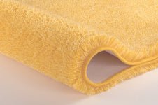 Nahaufnahme gelber Badematte mit weichem, hochflorigem Teppichrand Detail