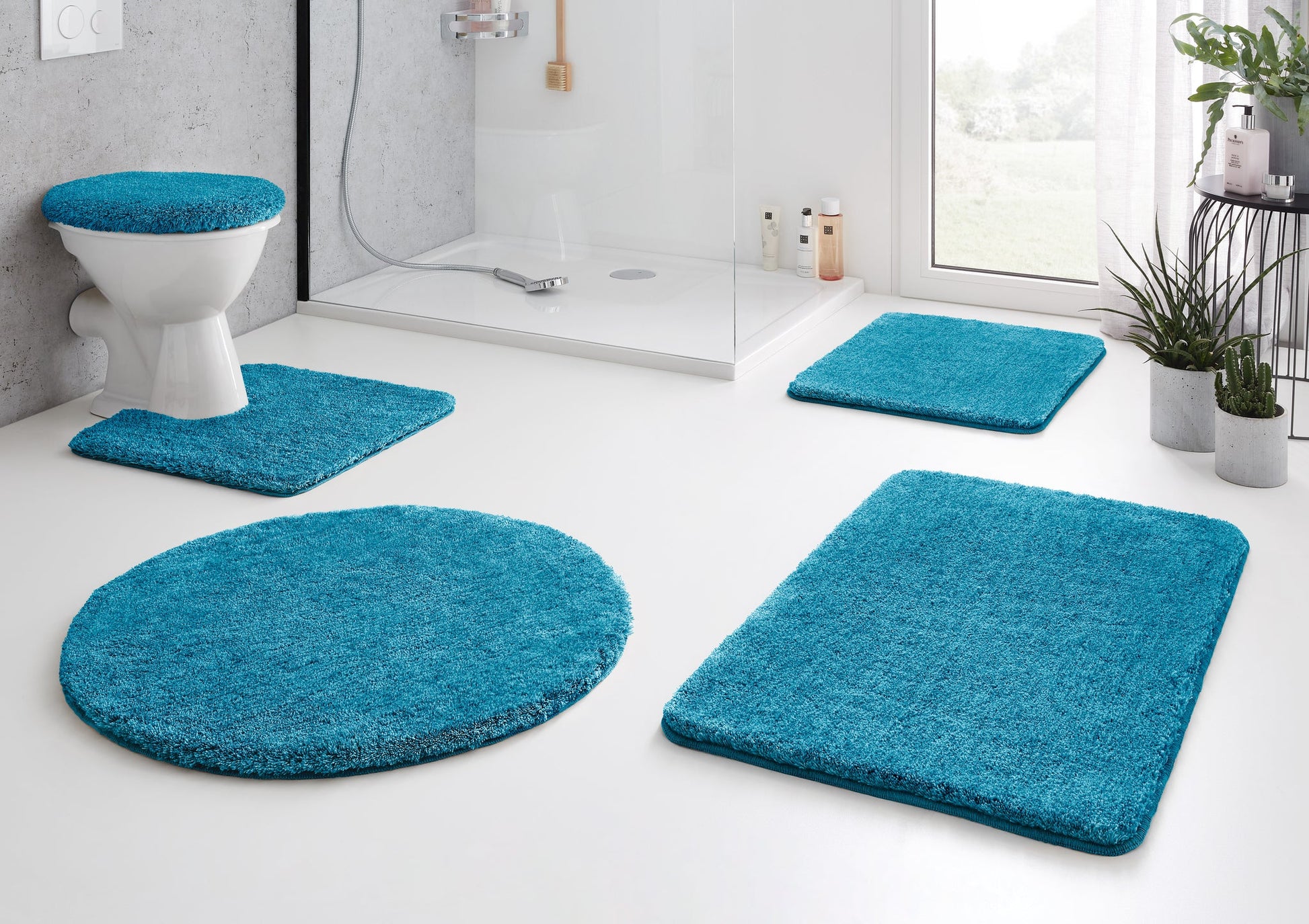 Badteppich RELAX Pazifik 50 x 80 cm in Türkis vor Dusche in modernem Bad mit WC und Pflanzen.