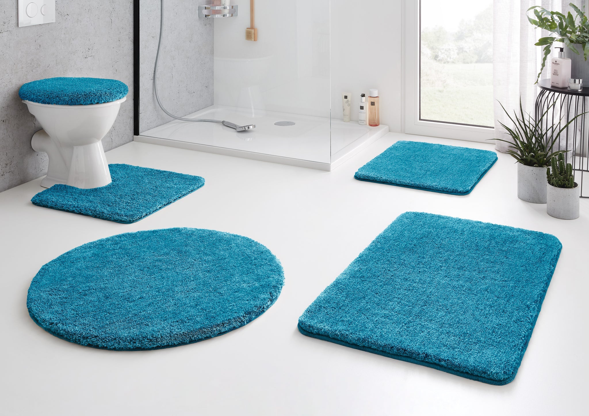 Badteppich RELAX Pazifik 50 x 80 cm in Türkis vor Dusche in modernem Bad mit WC und Pflanzen.