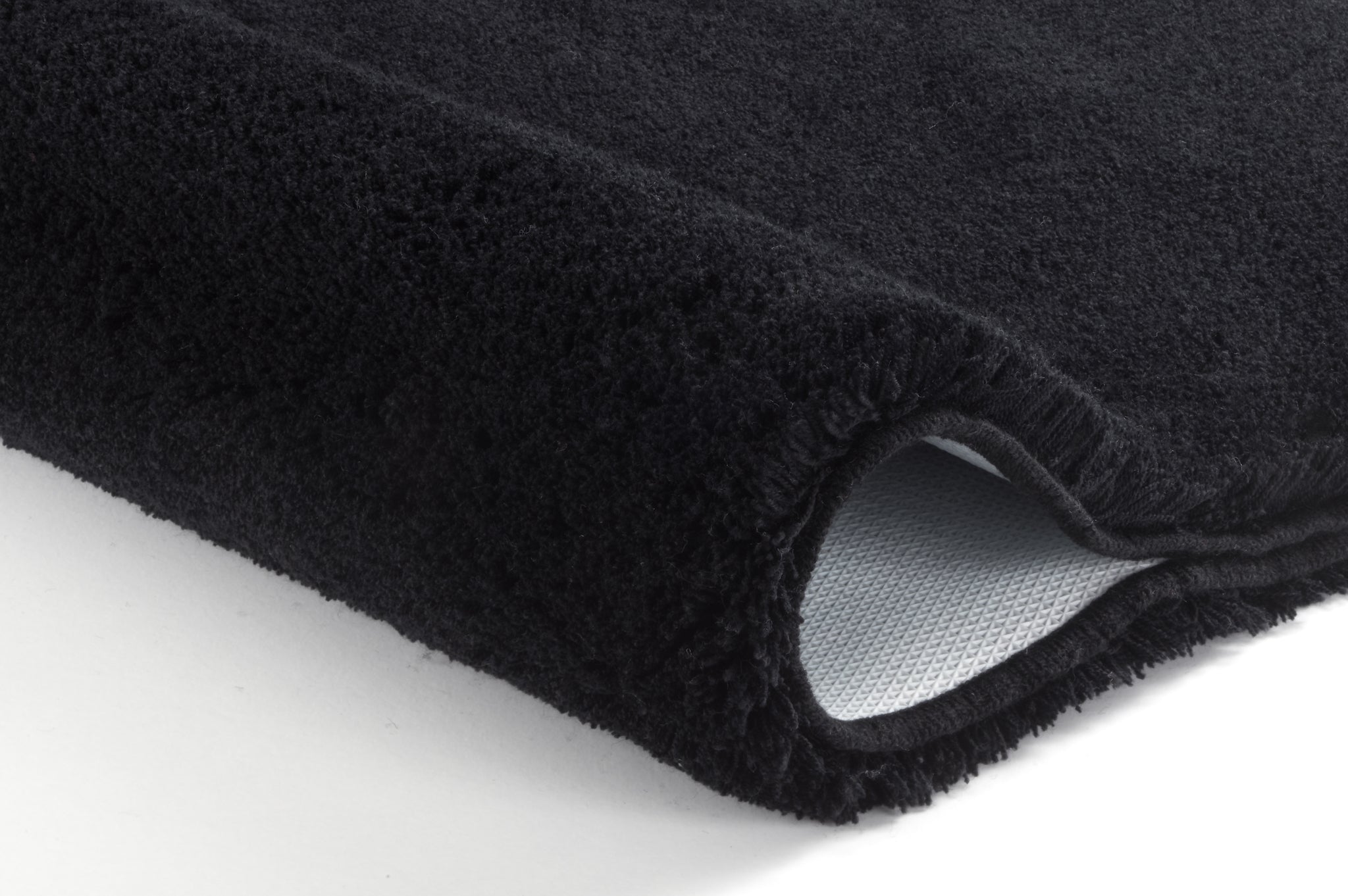 Badteppich RELAX Schwarz 50 x 80 cm liegt gefaltet, Nahaufnahme von Flor und rutschhemmender Rückseite.
