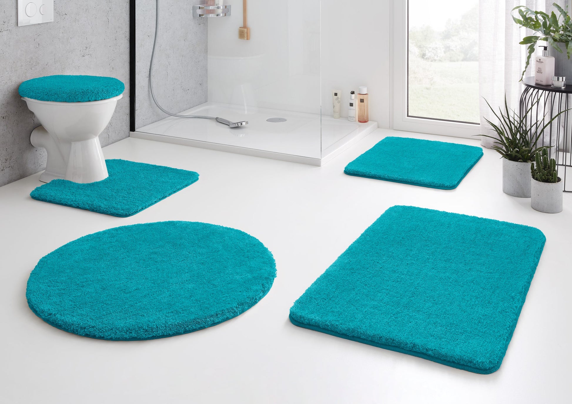 Badteppich RELAX Türkis 60 x 100 cm liegt in modernem Bad mit passender Badematte vor Dusche und WC.