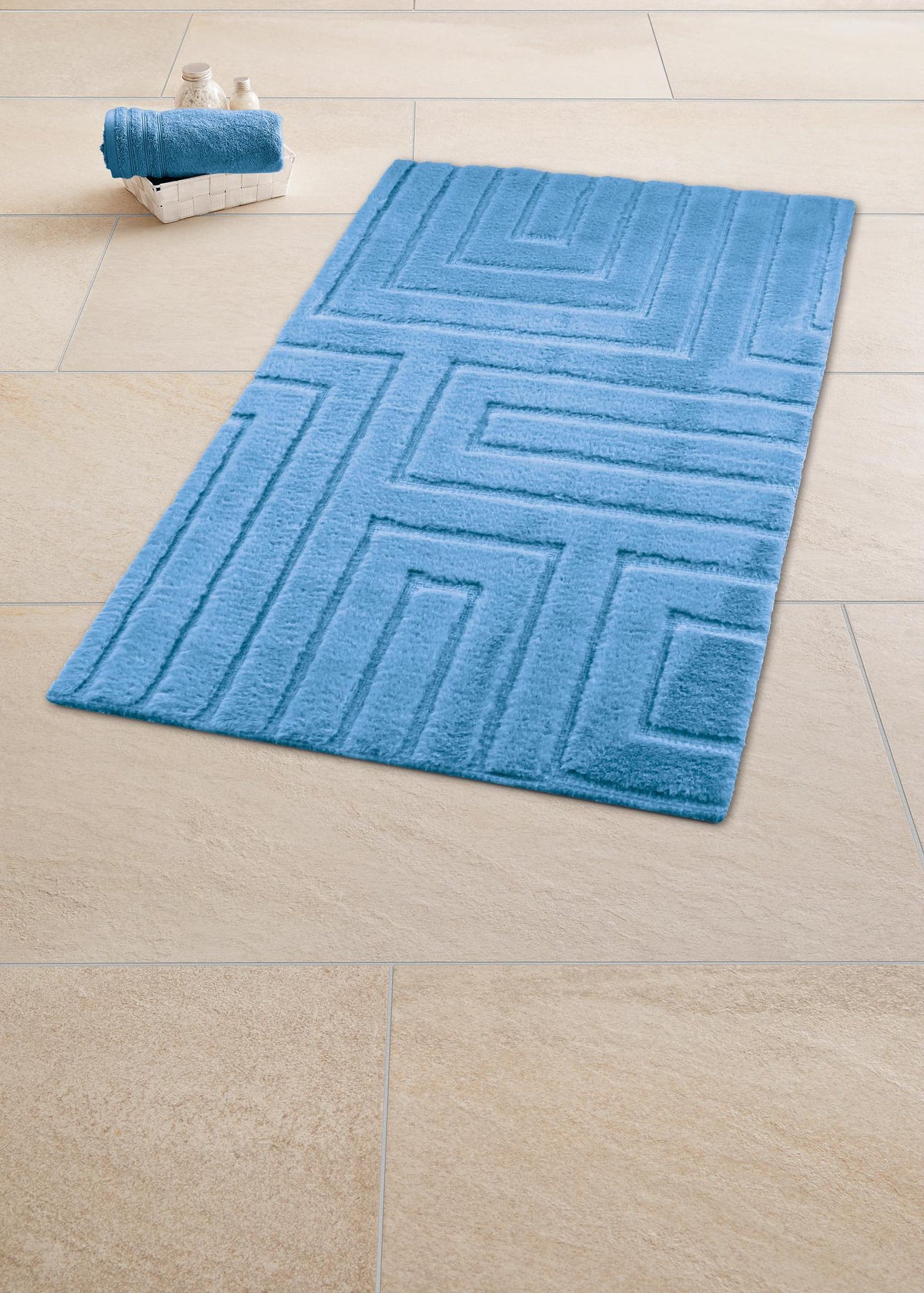 Blauer Badteppich mit Muster auf Fliesenboden, daneben Korb mit Handtuch.