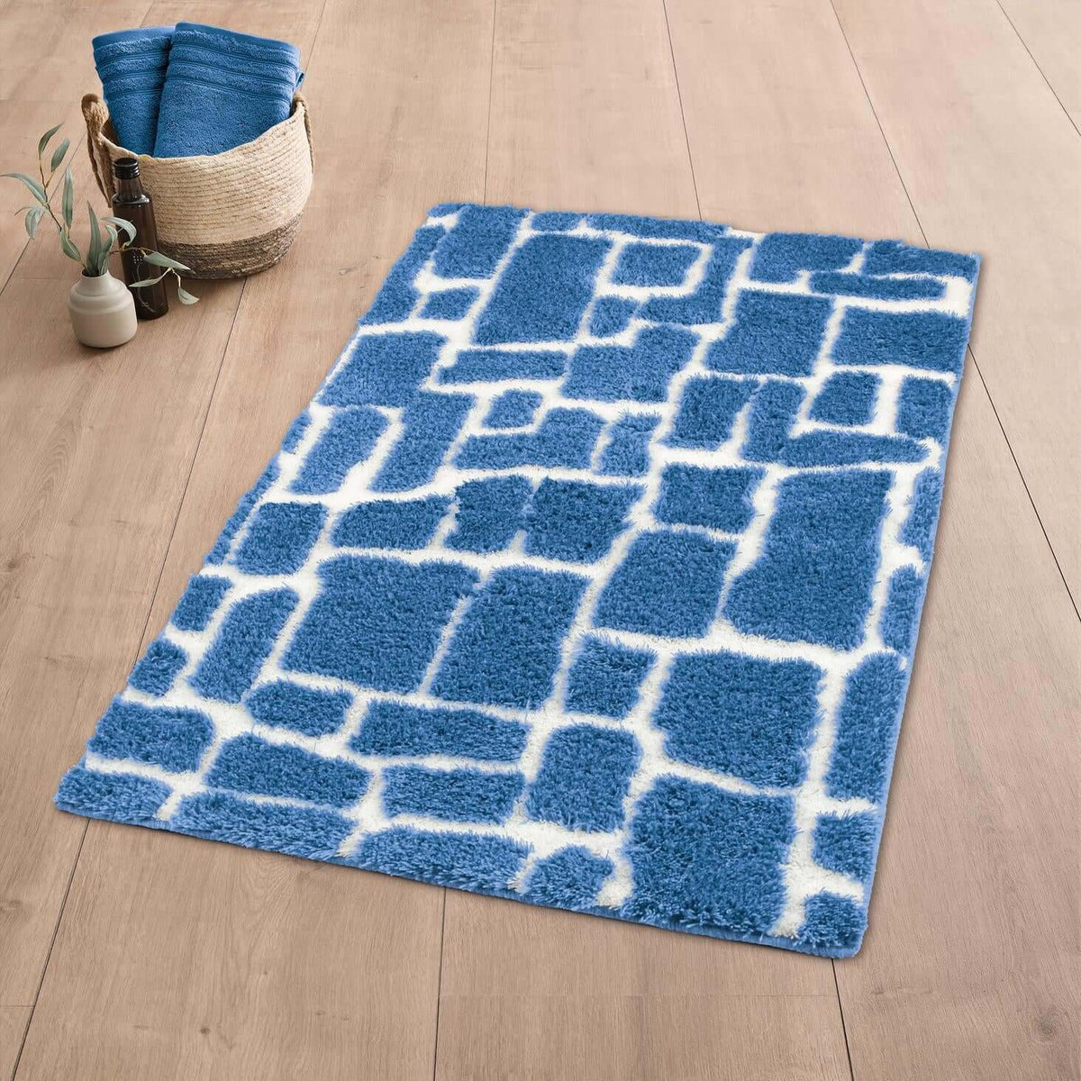 Blauer Badteppich mit Muster auf Holzoptikboden neben Korb und Deko.