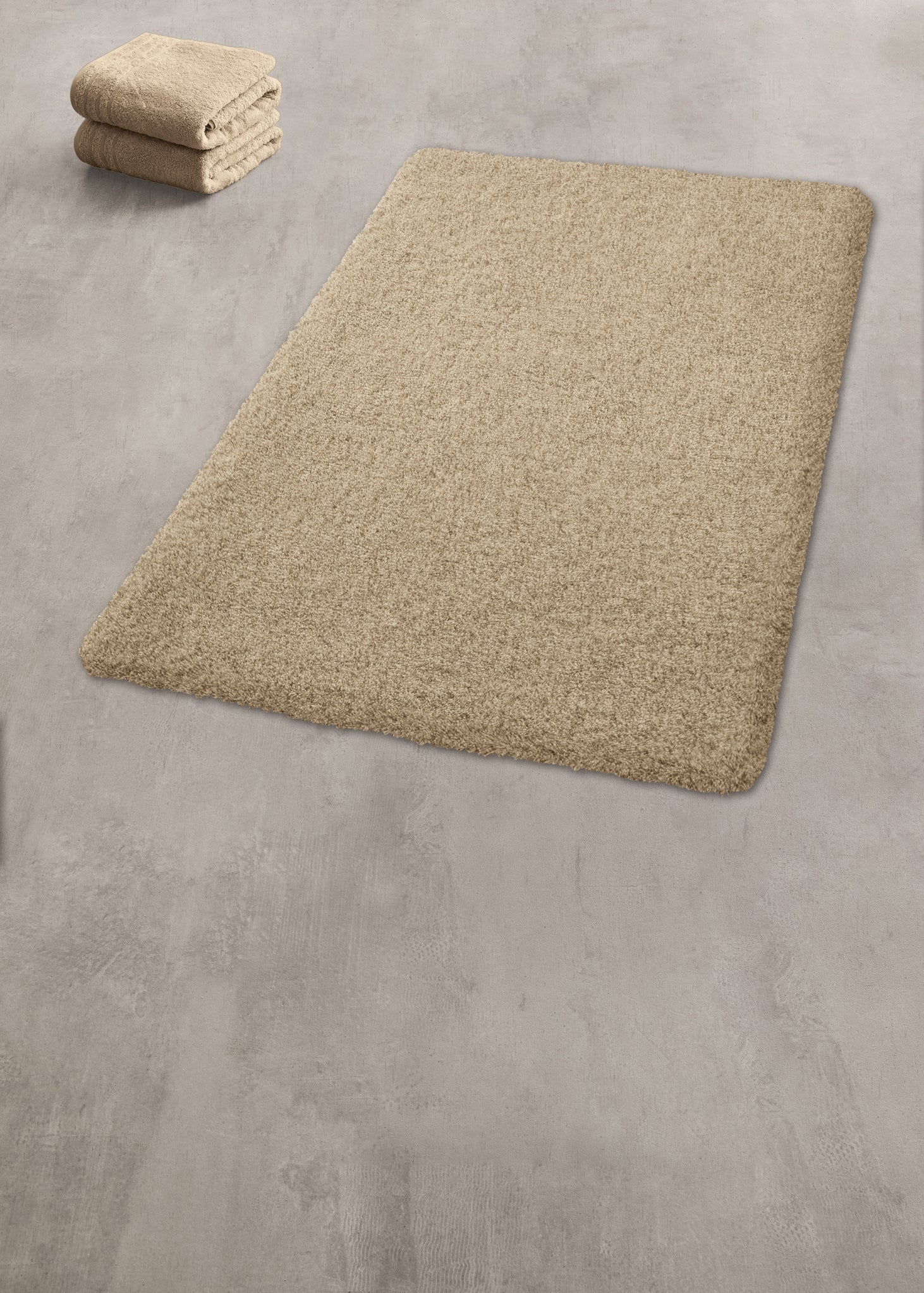 Beiger Badteppich mit passenden gefalteten Handtüchern auf grauem Boden