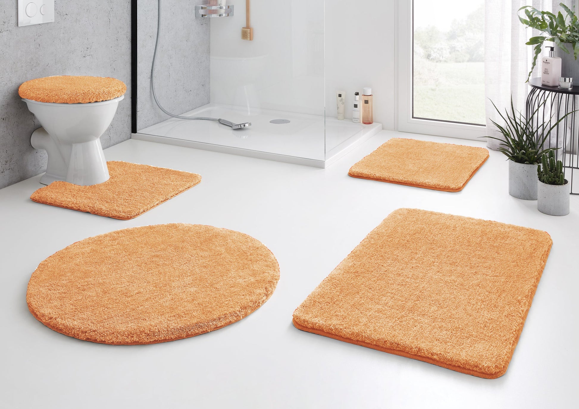 Badteppich-Set RELAX Peach mit Badteppichen vor Dusche, WC und Pflanzen im hellen modernen Bad.
