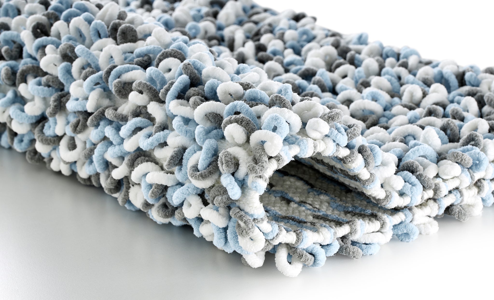 Gefalteter Badteppich SLING Opal 55 x 65 cm mit weicher, blau-grau-weißer Schlaufenstruktur auf Tisch.