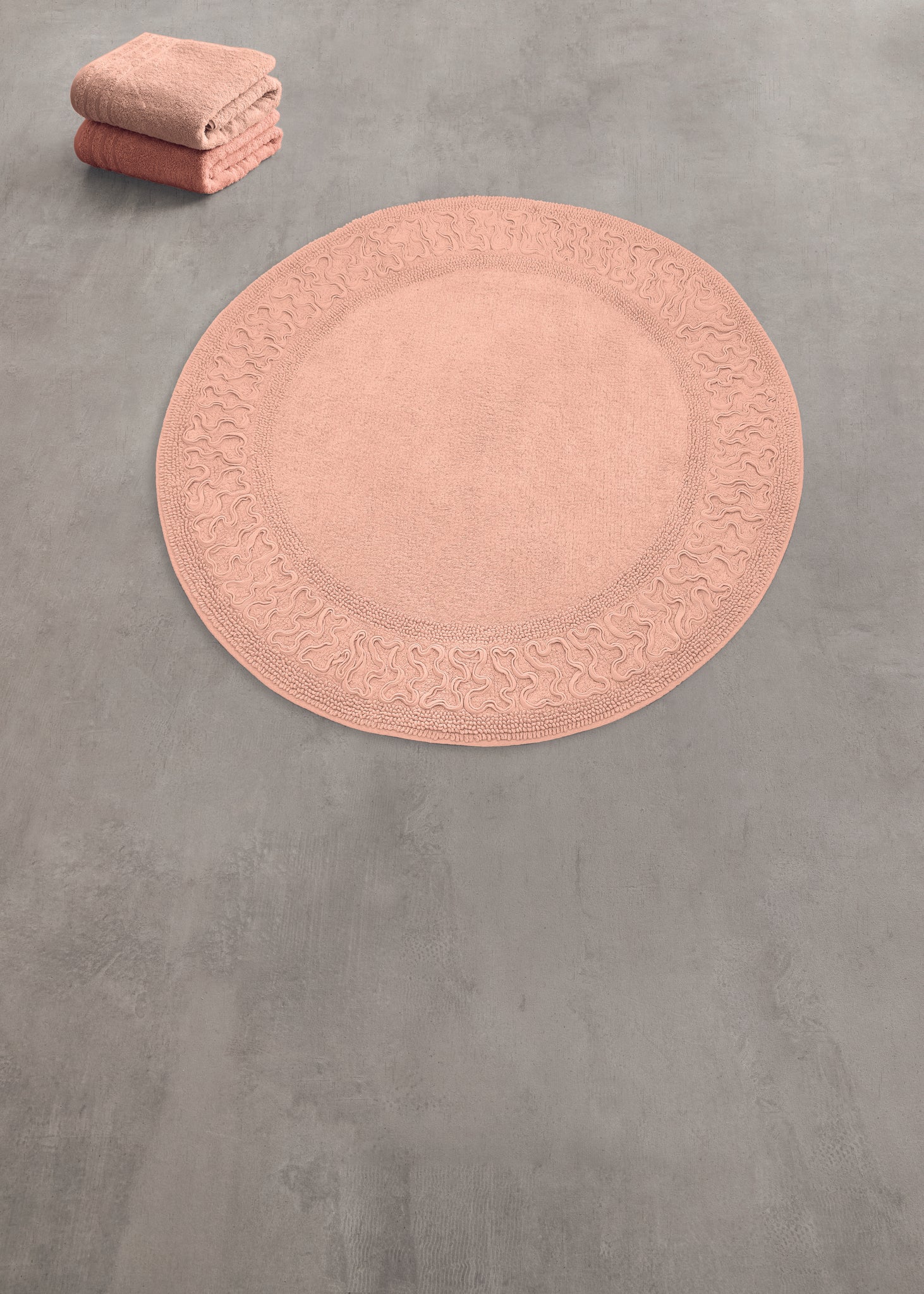 Runder rosa Badteppich mit Muster und passenden Handtüchern daneben