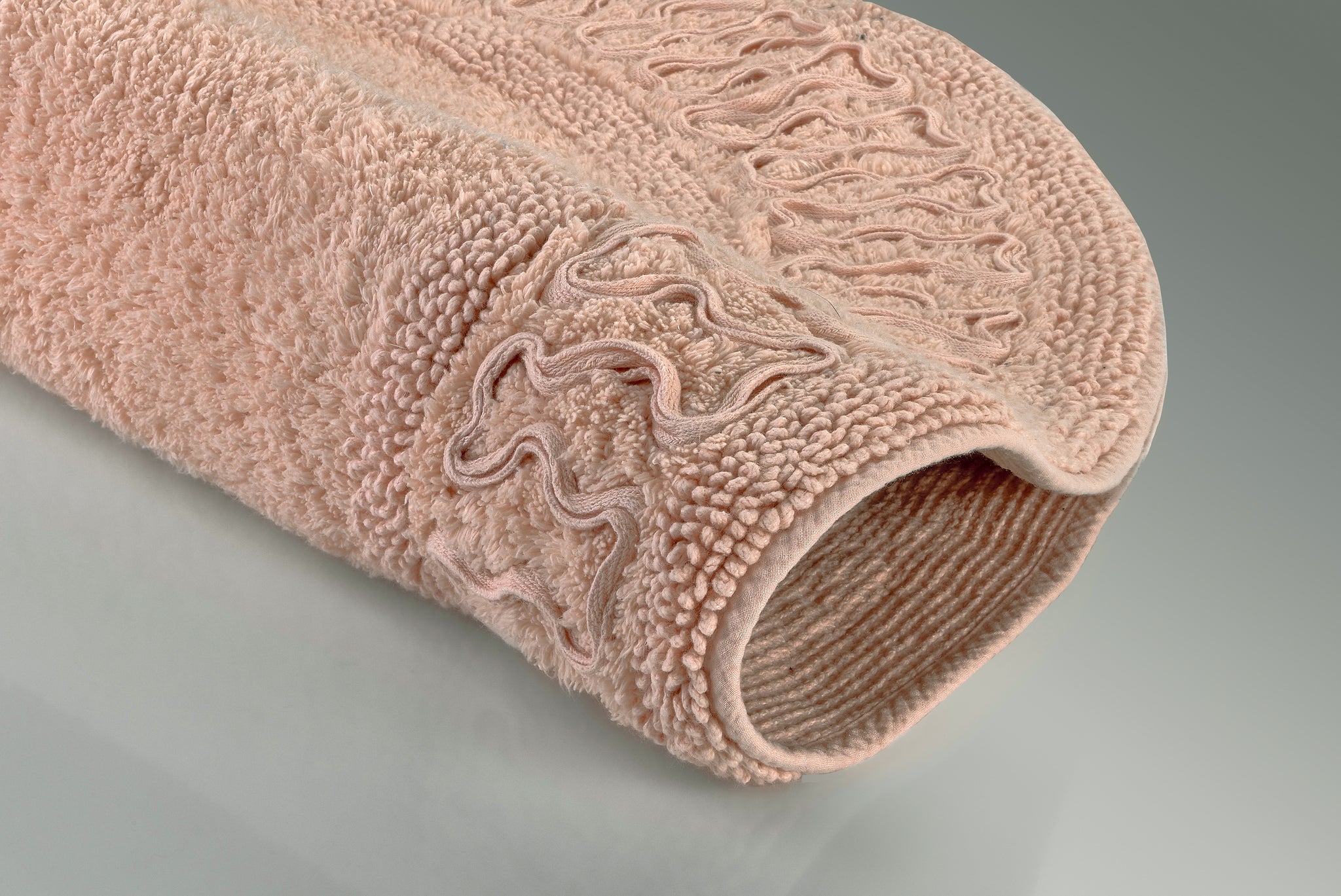 Rosafarbene Badematte mit Strukturmuster, seitlich zusammengerollt