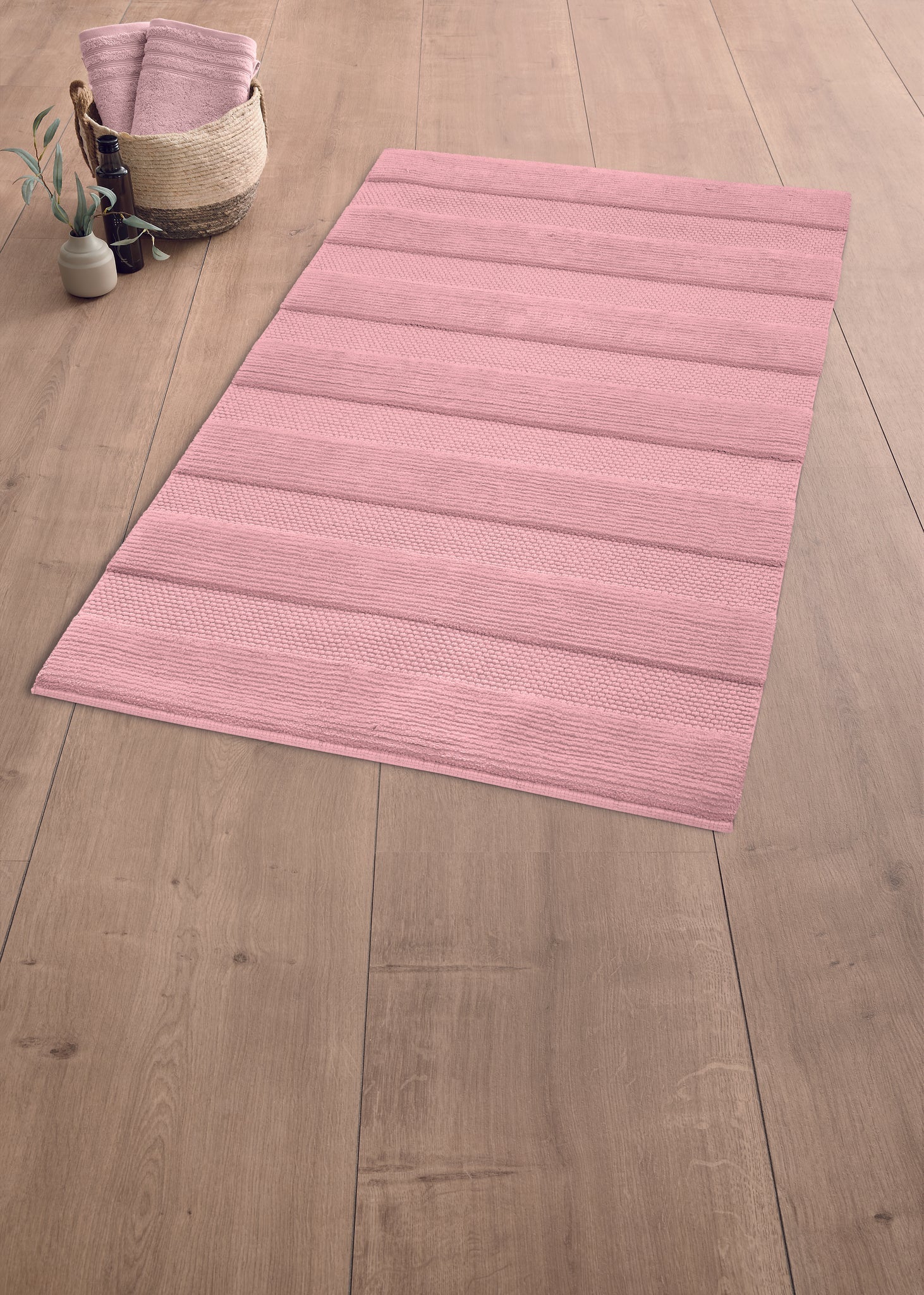Rosa Badteppich auf Holzfußboden mit Korb und gefalteten Handtüchern