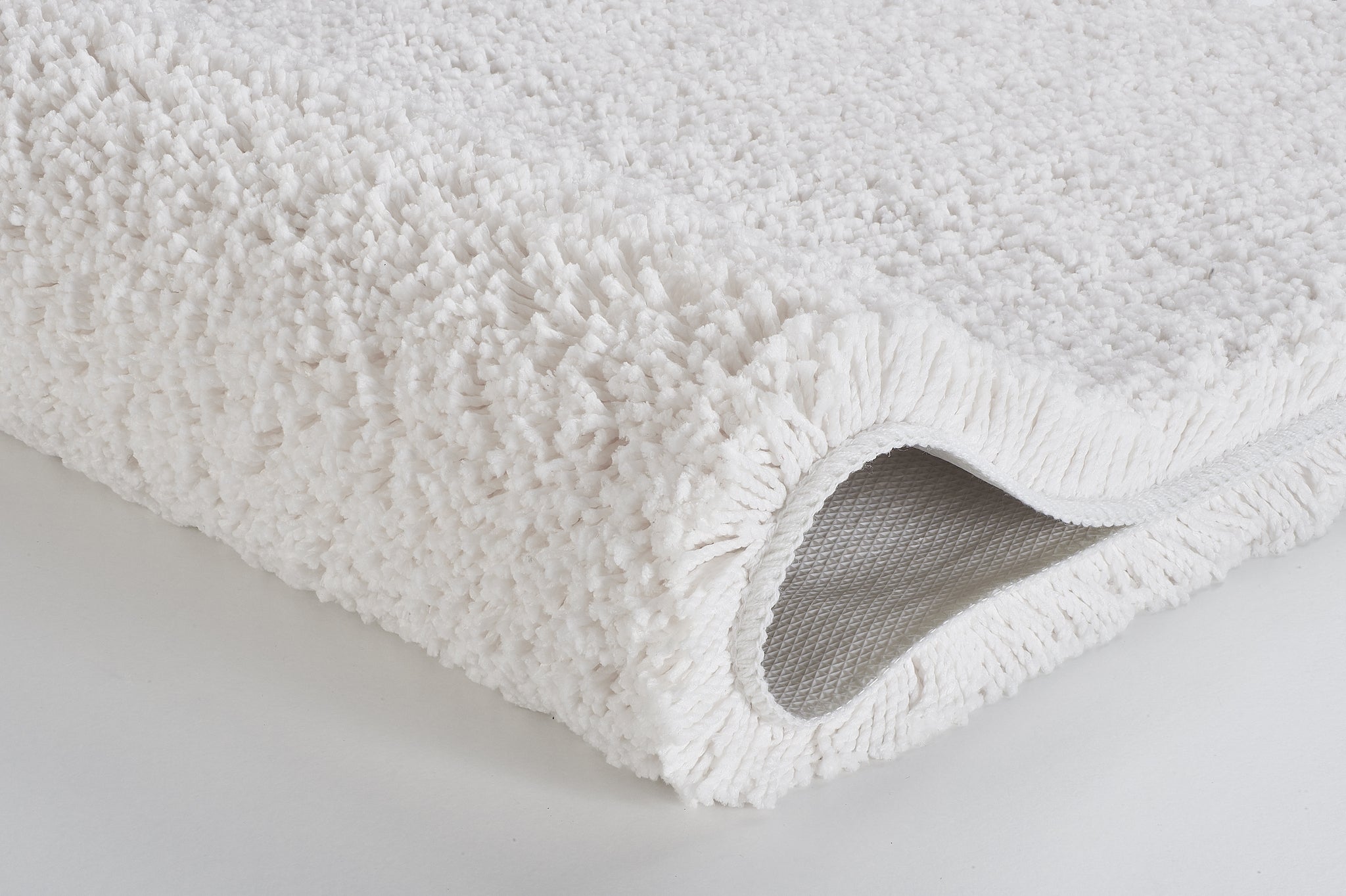 Weißer, flauschiger Badteppich in Nahaufnahme, gerollte Kante sichtbar