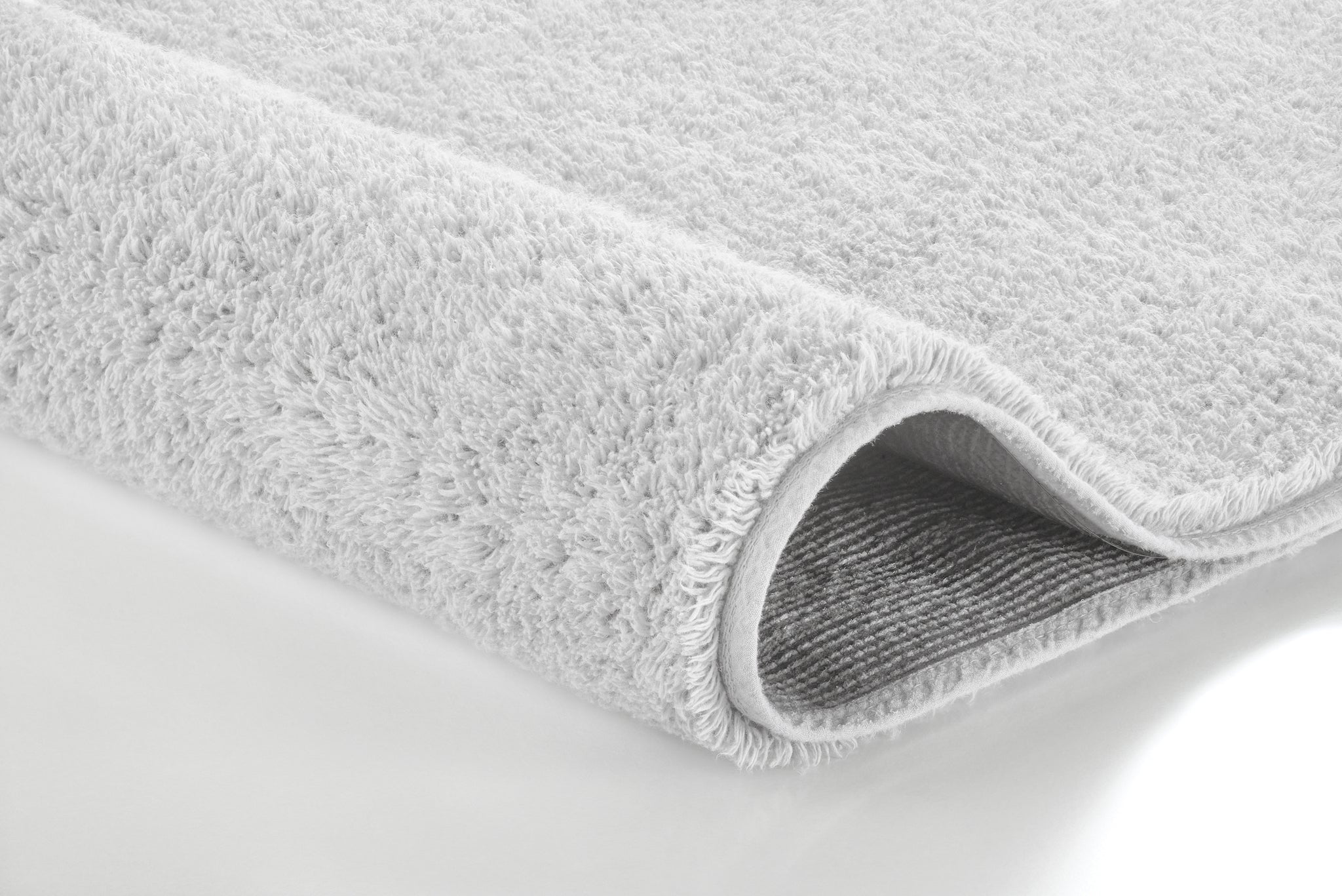 Nahaufnahme des weißen Badteppichs VITA 50 x 80 cm mit weicher, gerollter Kante auf hellem Untergrund.