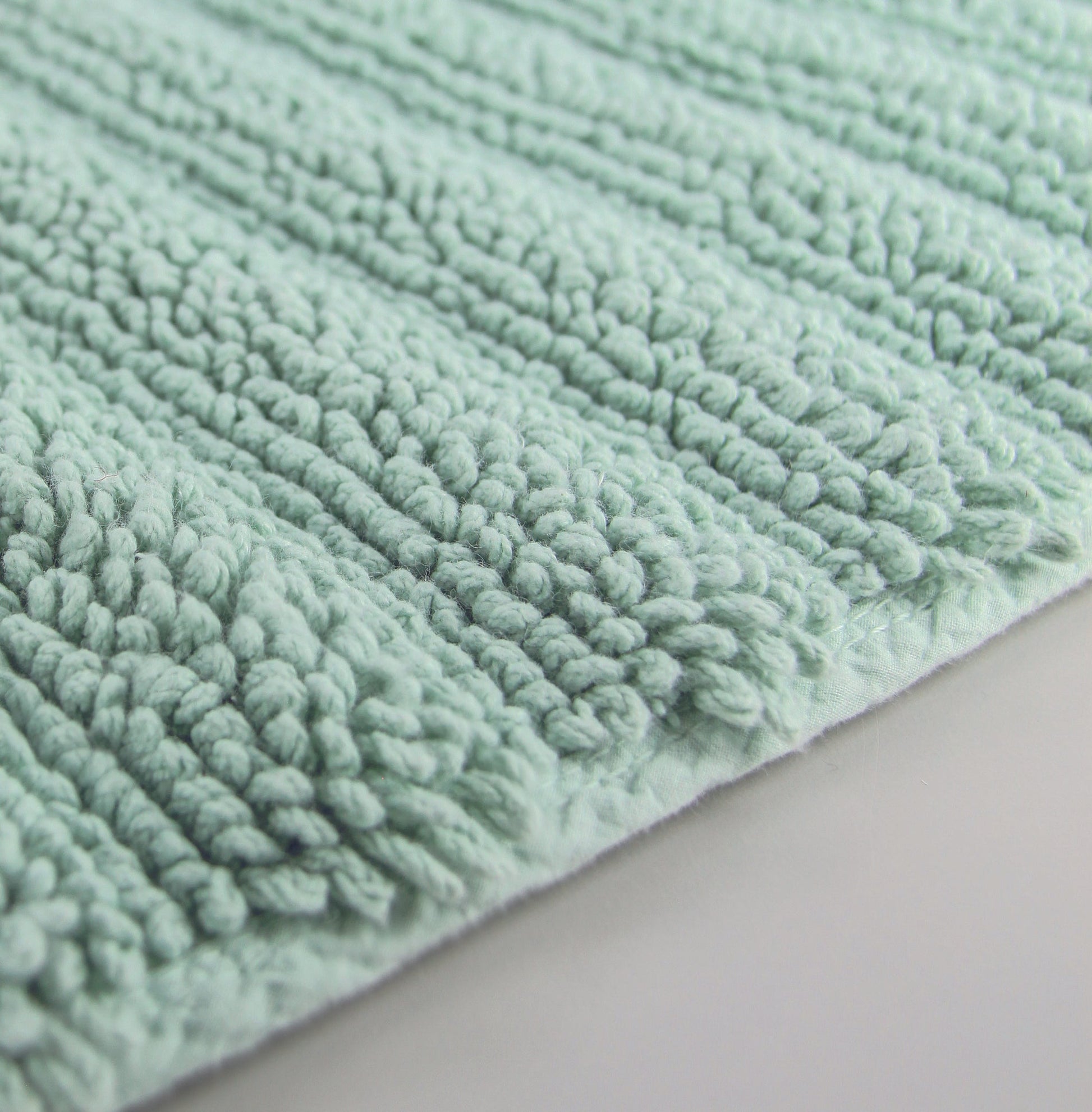 Nahaufnahme einer mintgrünen, strukturierten Badematte auf hellgrauem Boden