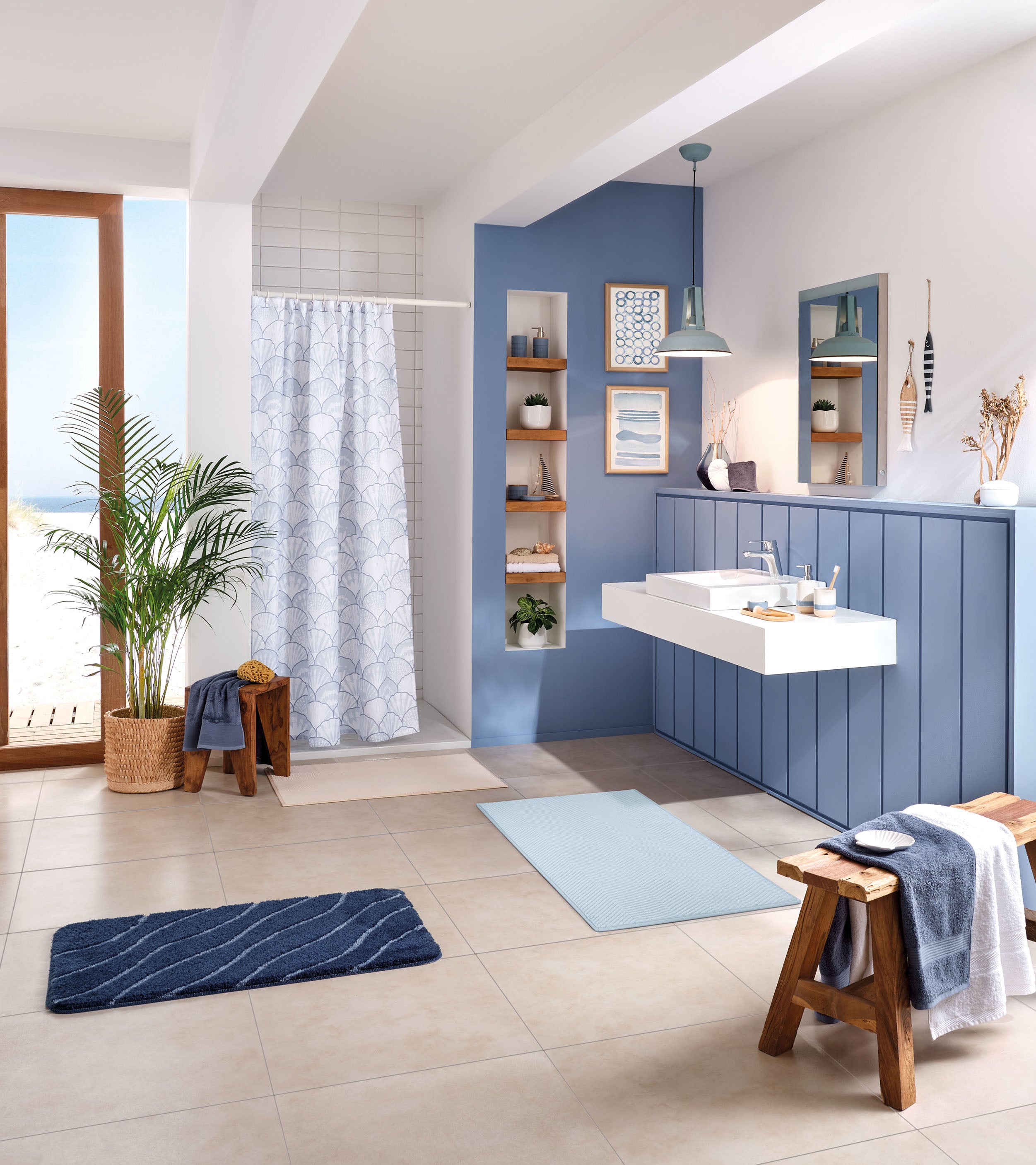 Modernes Badezimmer mit blauem Duschvorhang, maritimer Deko und Badteppichen in Sand- und Blautönen.