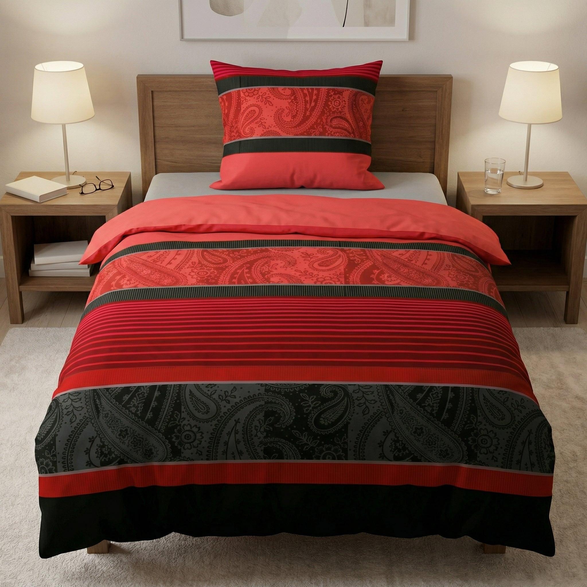 Rote Bettwäsche mit schwarzem Paisleymuster auf einem Holzbett.