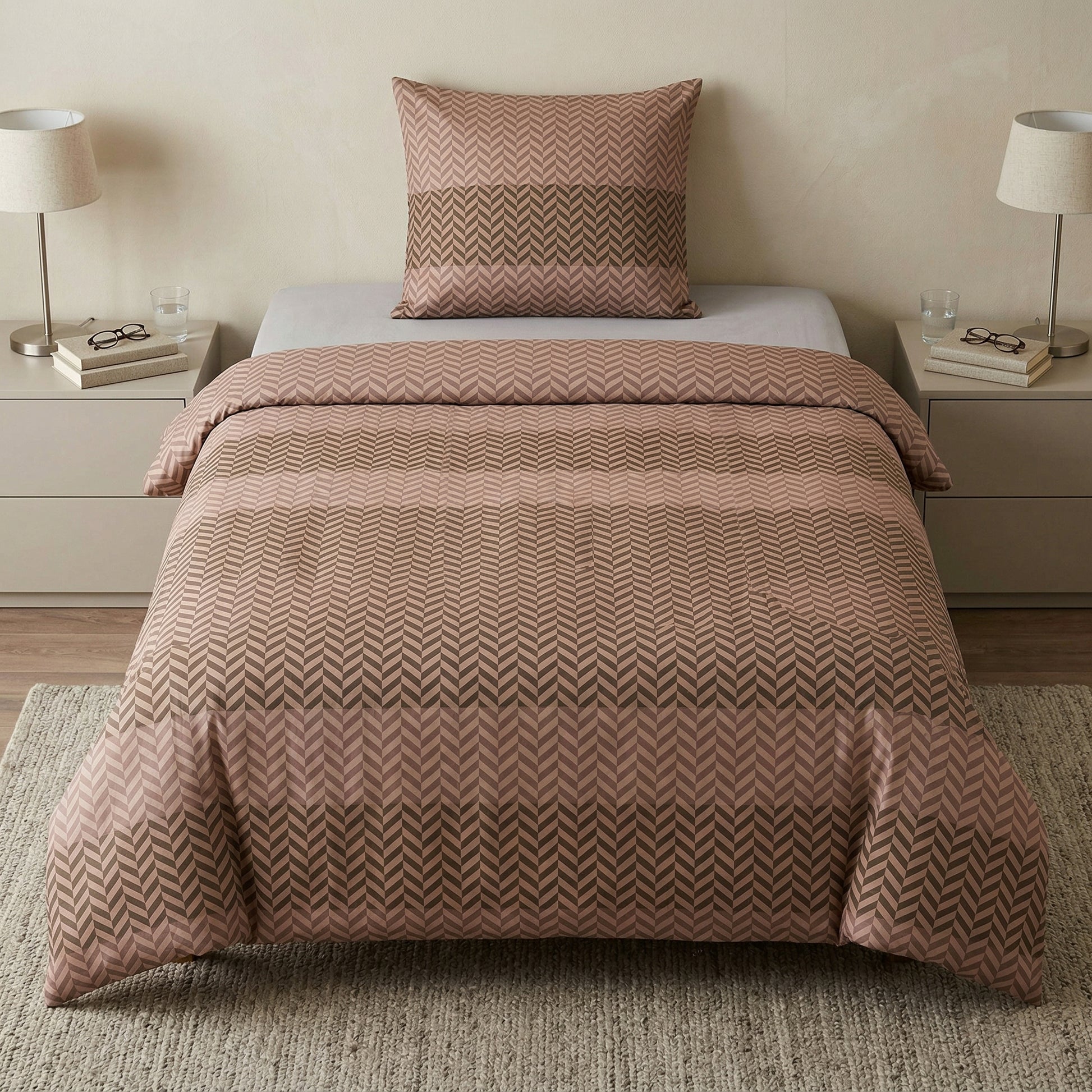 Rosé Bettwäsche im Zickzackmuster auf Bett zwischen zwei Nachttischen.