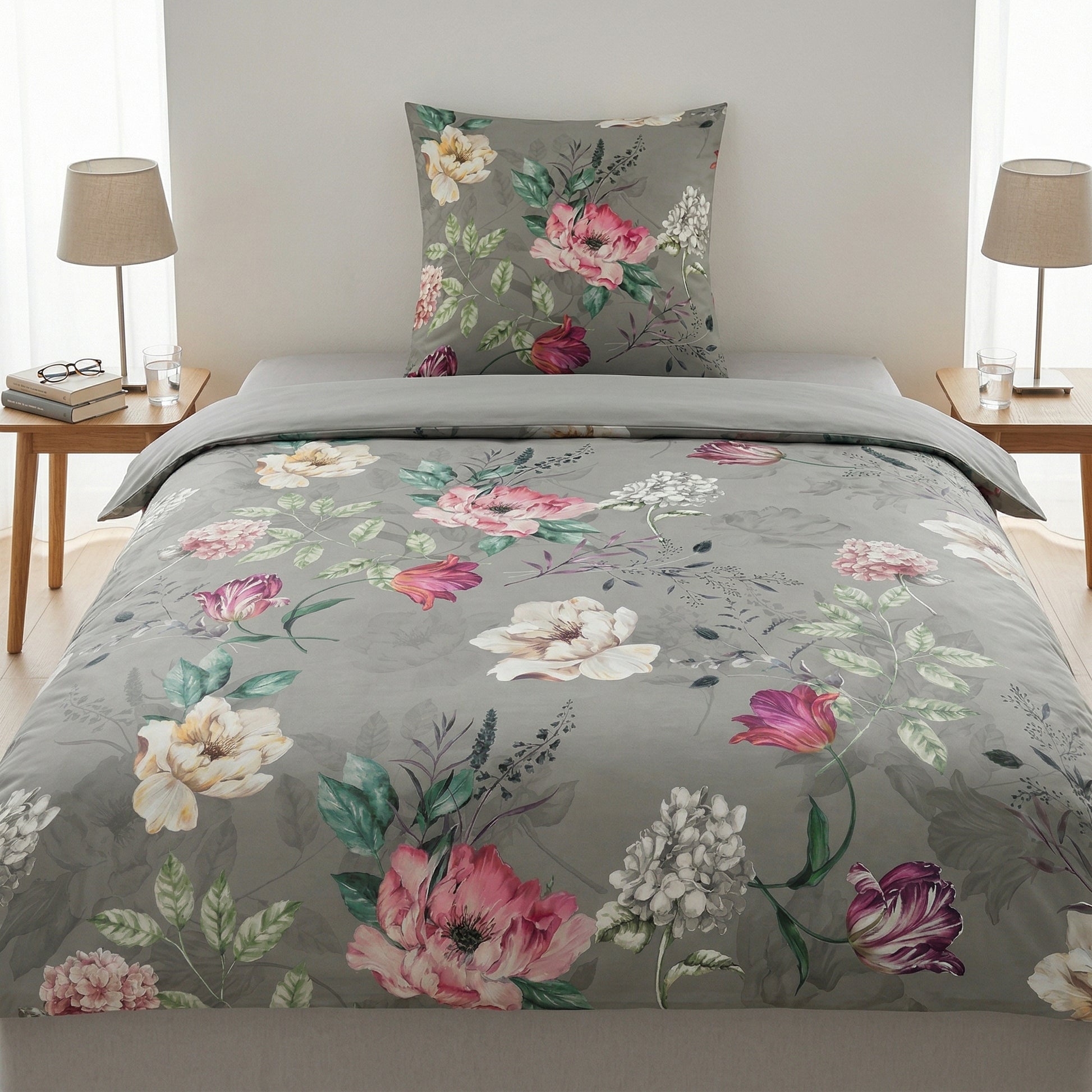 Graue Bettwäsche mit Blumenmuster auf Bett, Nachttische mit Lampen.