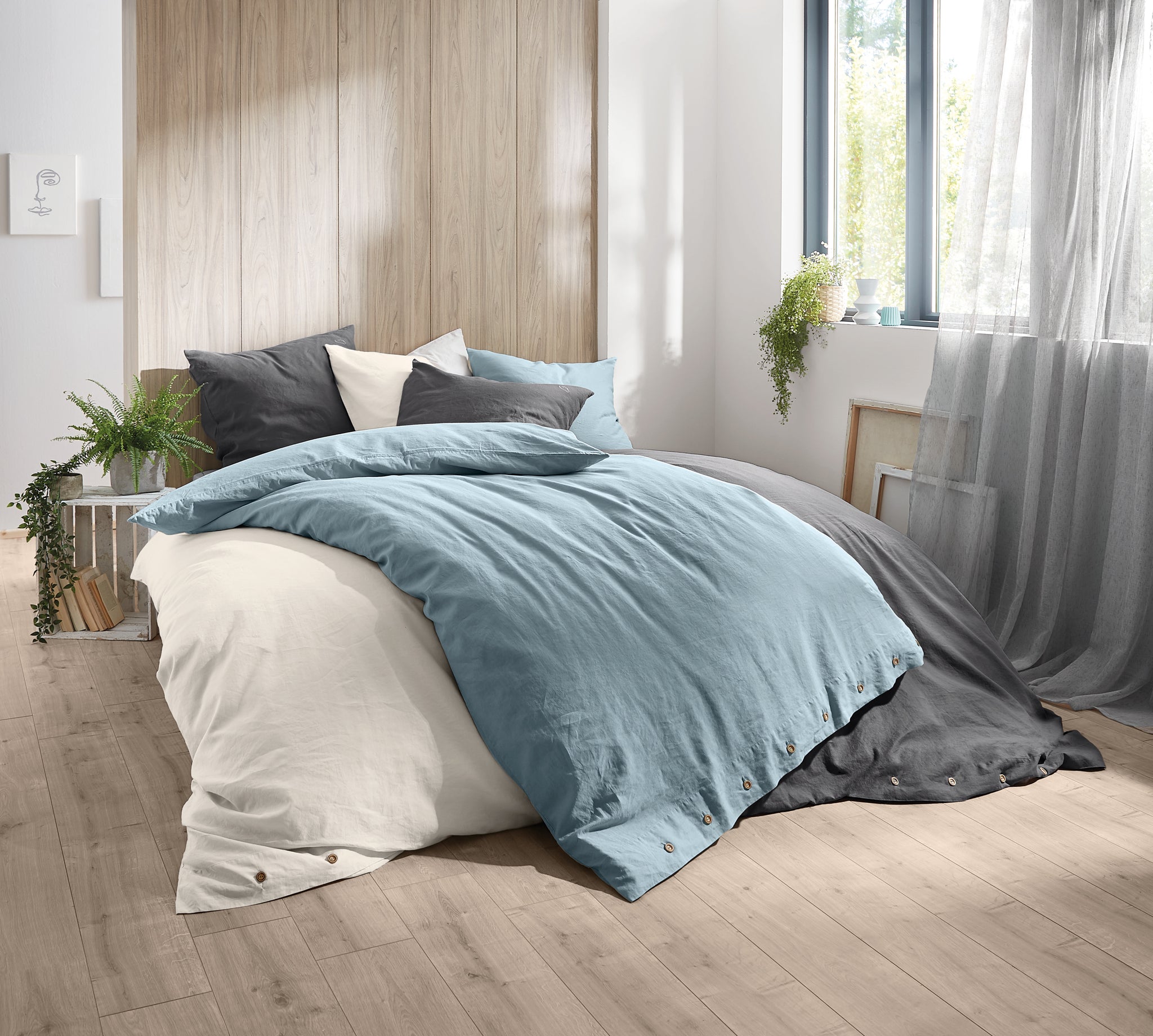 Gemütliches Bett mit blauer, grauer und weißer Bettwäsche im Tageslicht