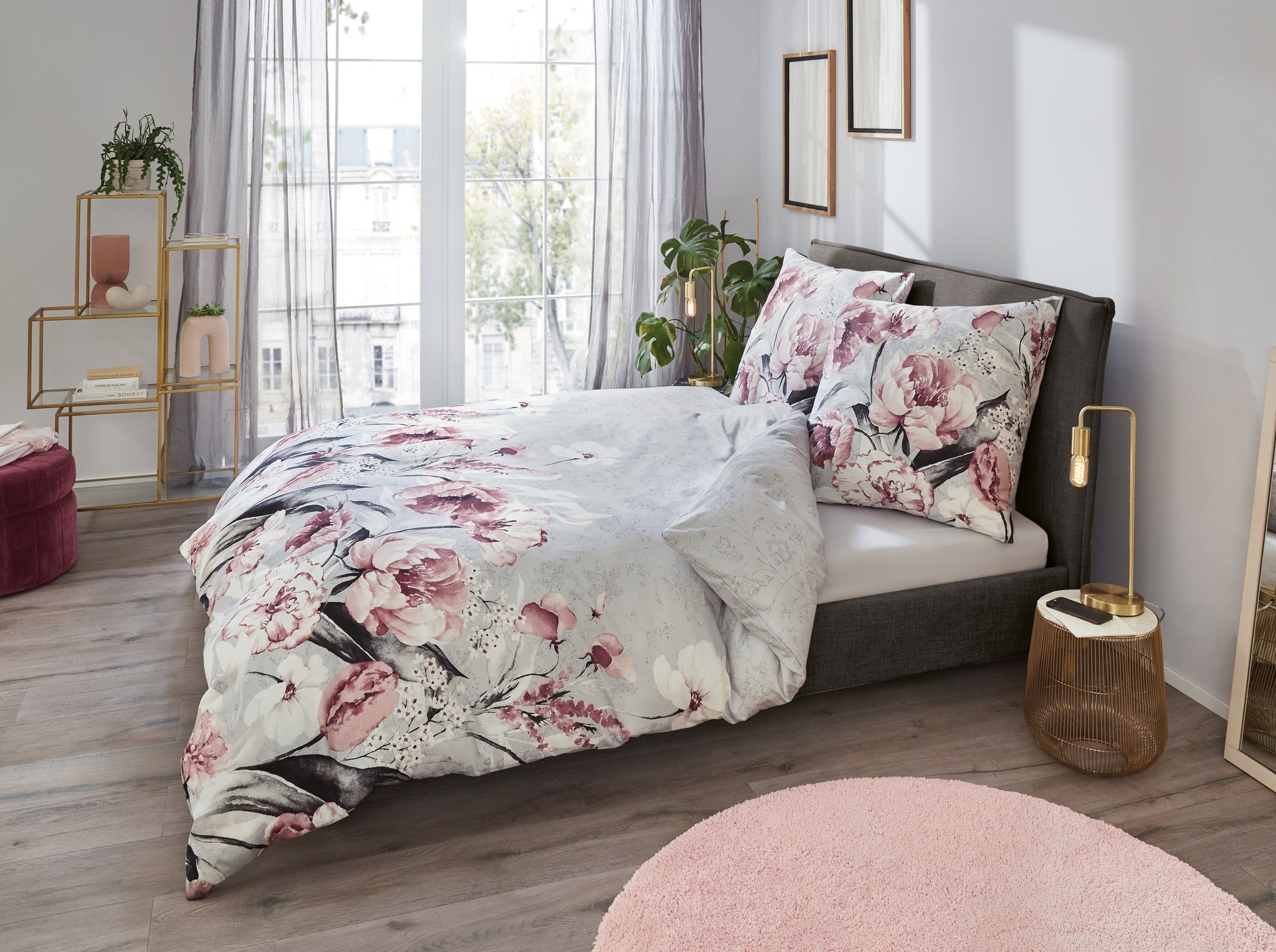 Graues Boxspringbett mit rosafarbener Blumenbettwäsche im hellen Zimmer