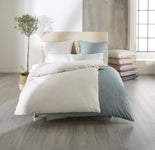 Doppelbett mit weiß-blauer Bettwäsche, Kissenstapel und Zimmerpflanze