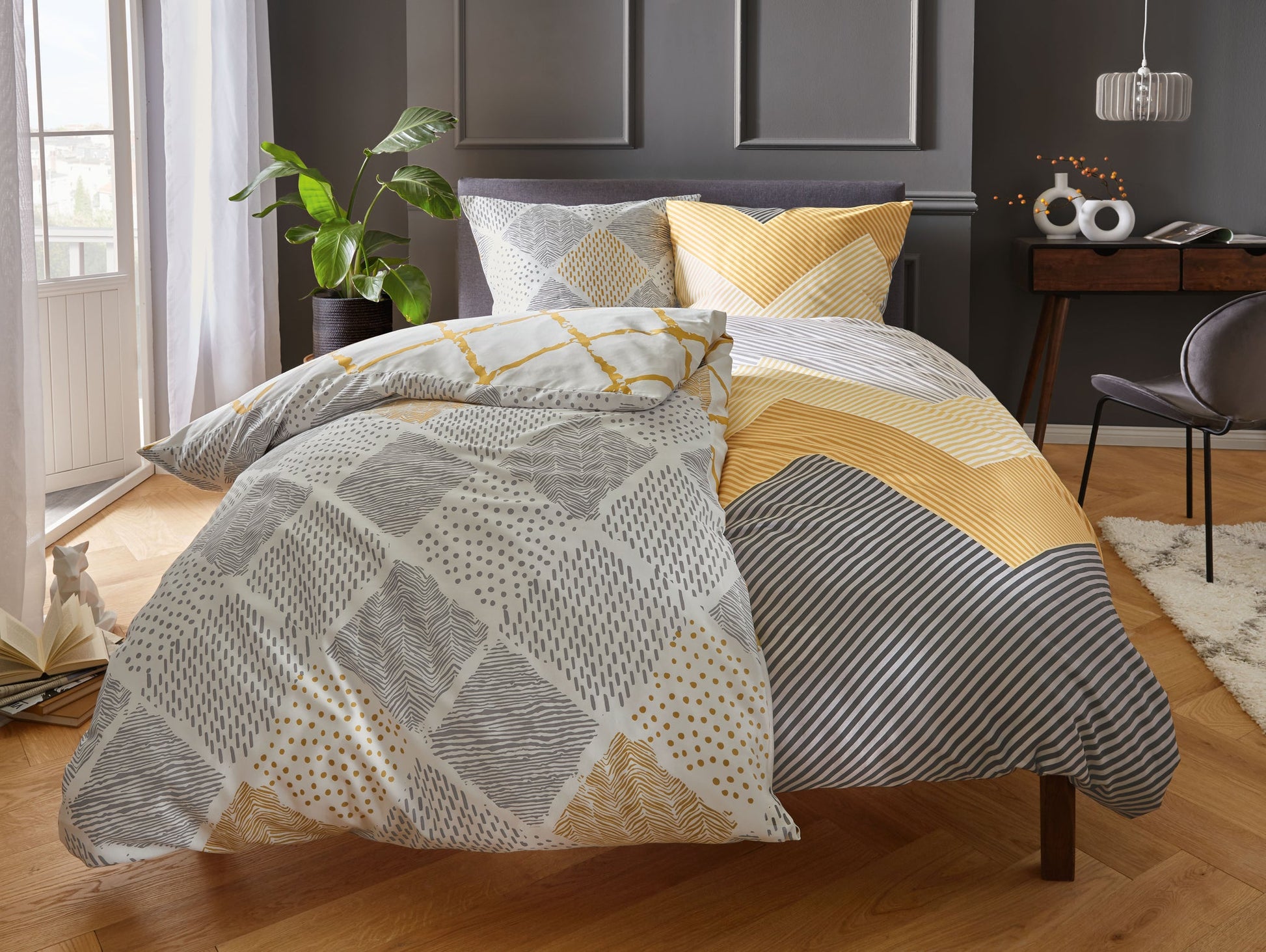Bett mit gelb-grauer gemusterter Bettwäsche in modernem Schlafzimmer