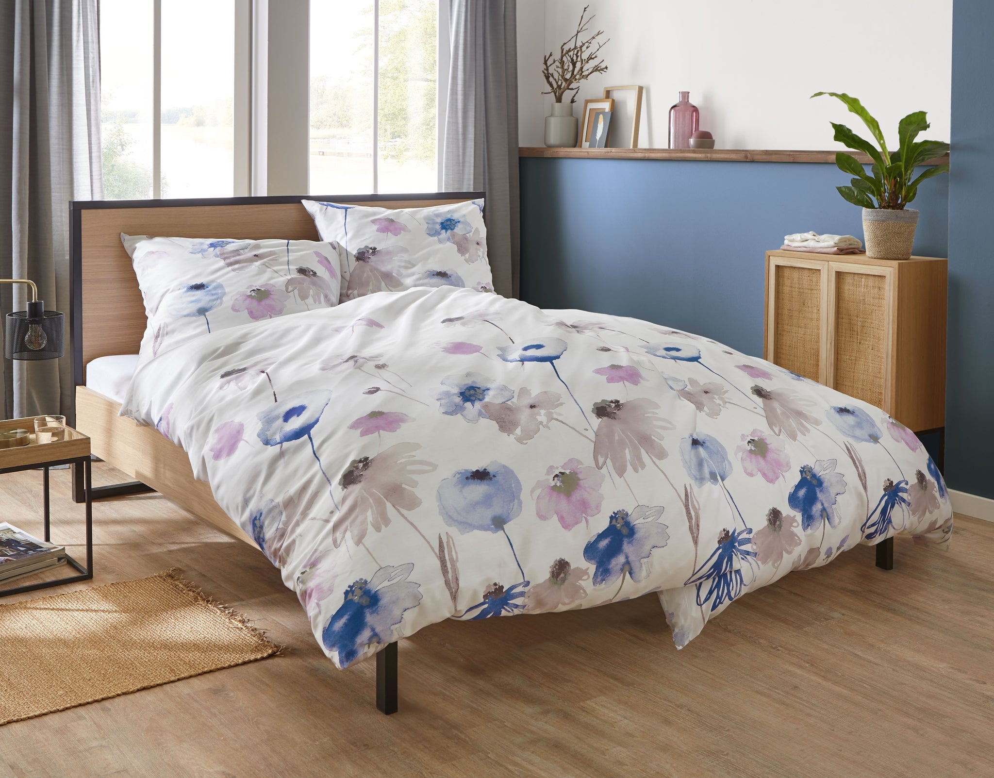 Bett mit weißer Bettwäsche mit Aquarell-Blumen in Blau und Rosa