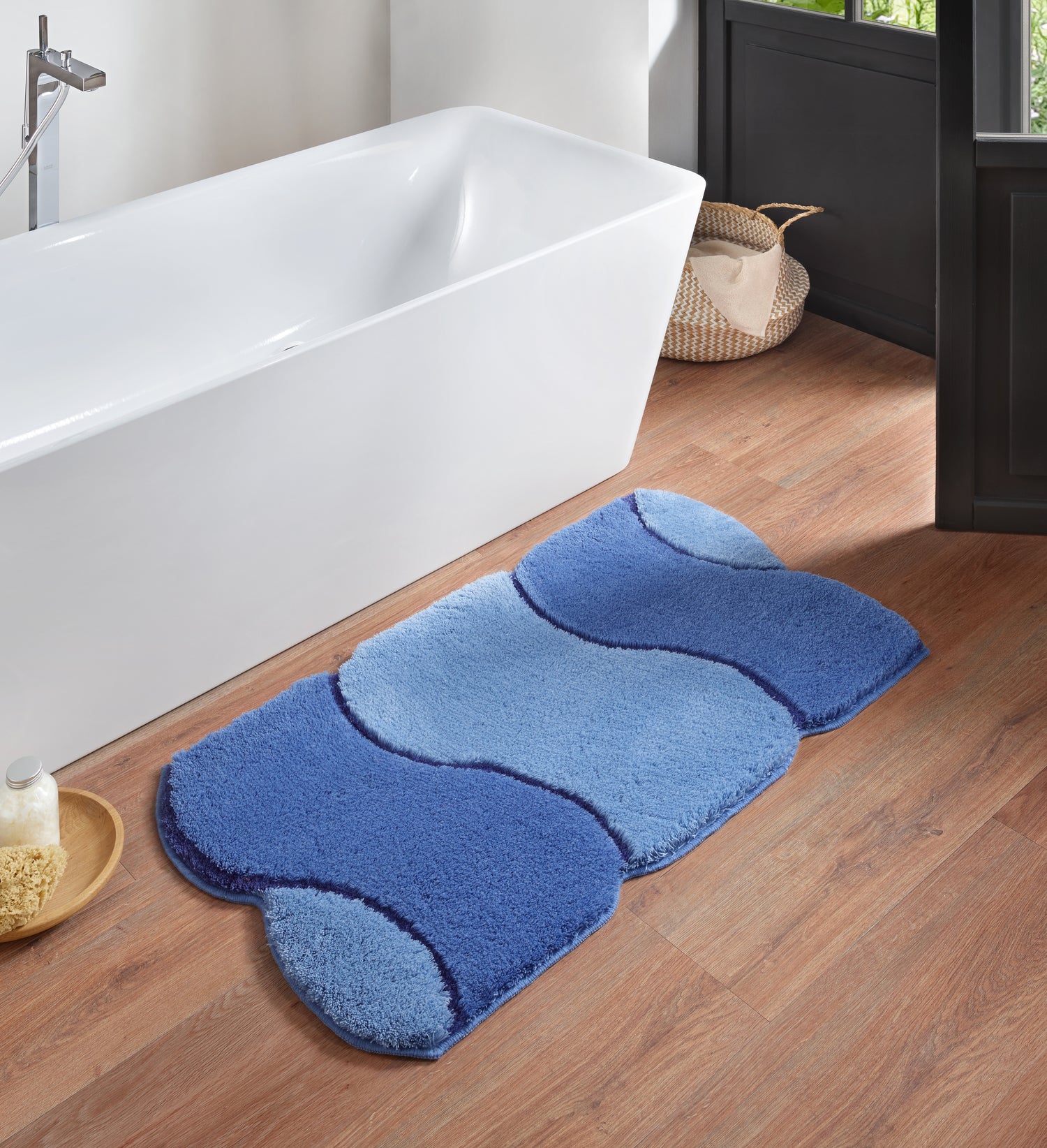 Badematte Kleine Wolke Creativo Arcata in Blautönen liegt vor einer Badewanne auf Holzfußboden.