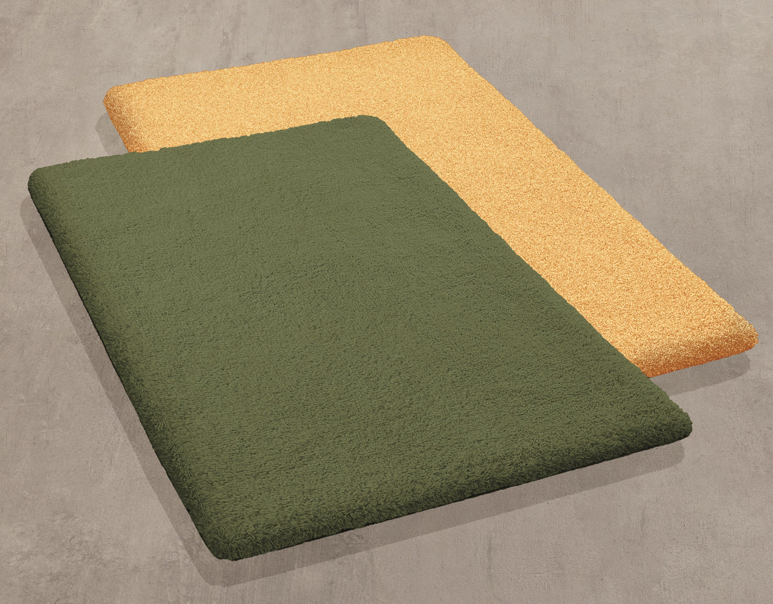 Zwei rechteckige Badteppiche in Olivgrün und Beige liegen auf einem grauen Boden.