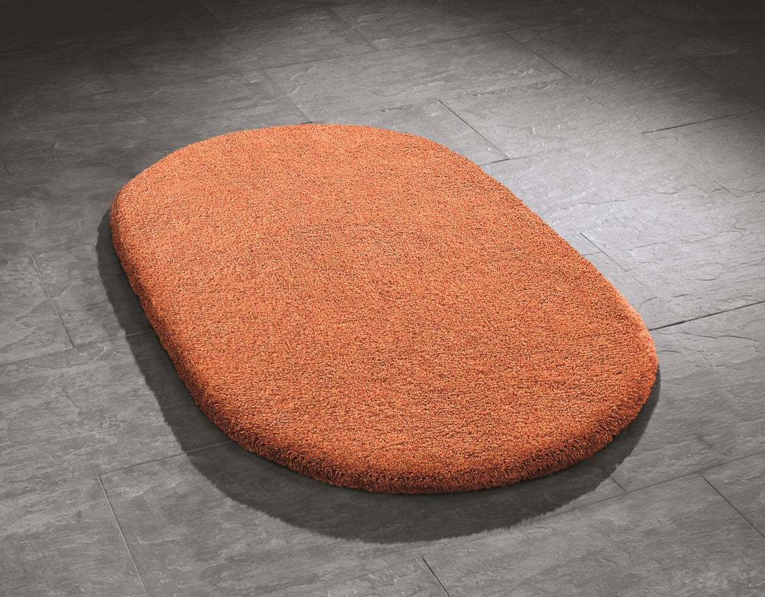 Ovaler Kleine Wolke Creativo Badteppich Relax in Orange auf grauen Badezimmerfliesen.