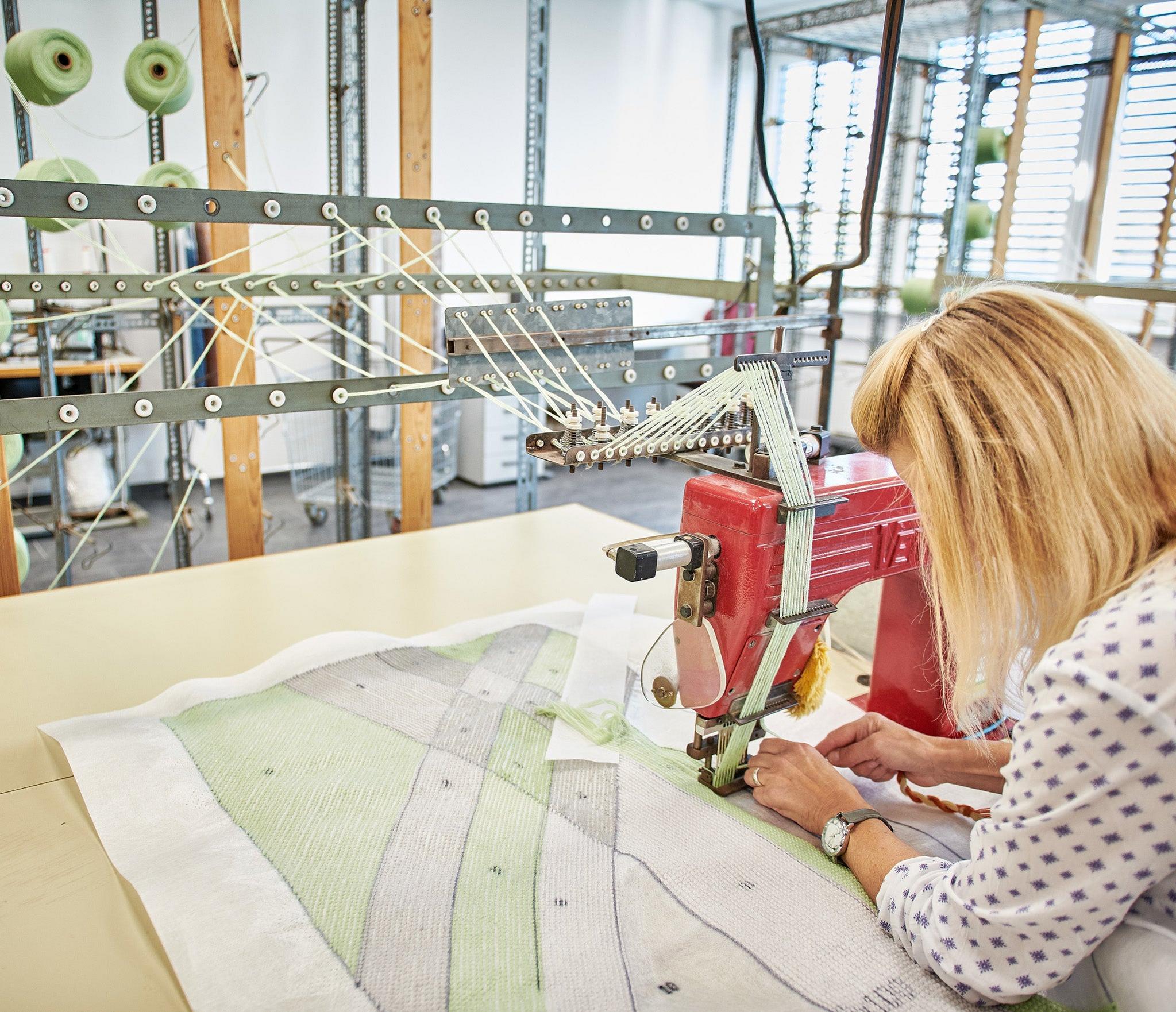 Frau näht grünes Badteppich-Design präzise an Industrienähmaschine