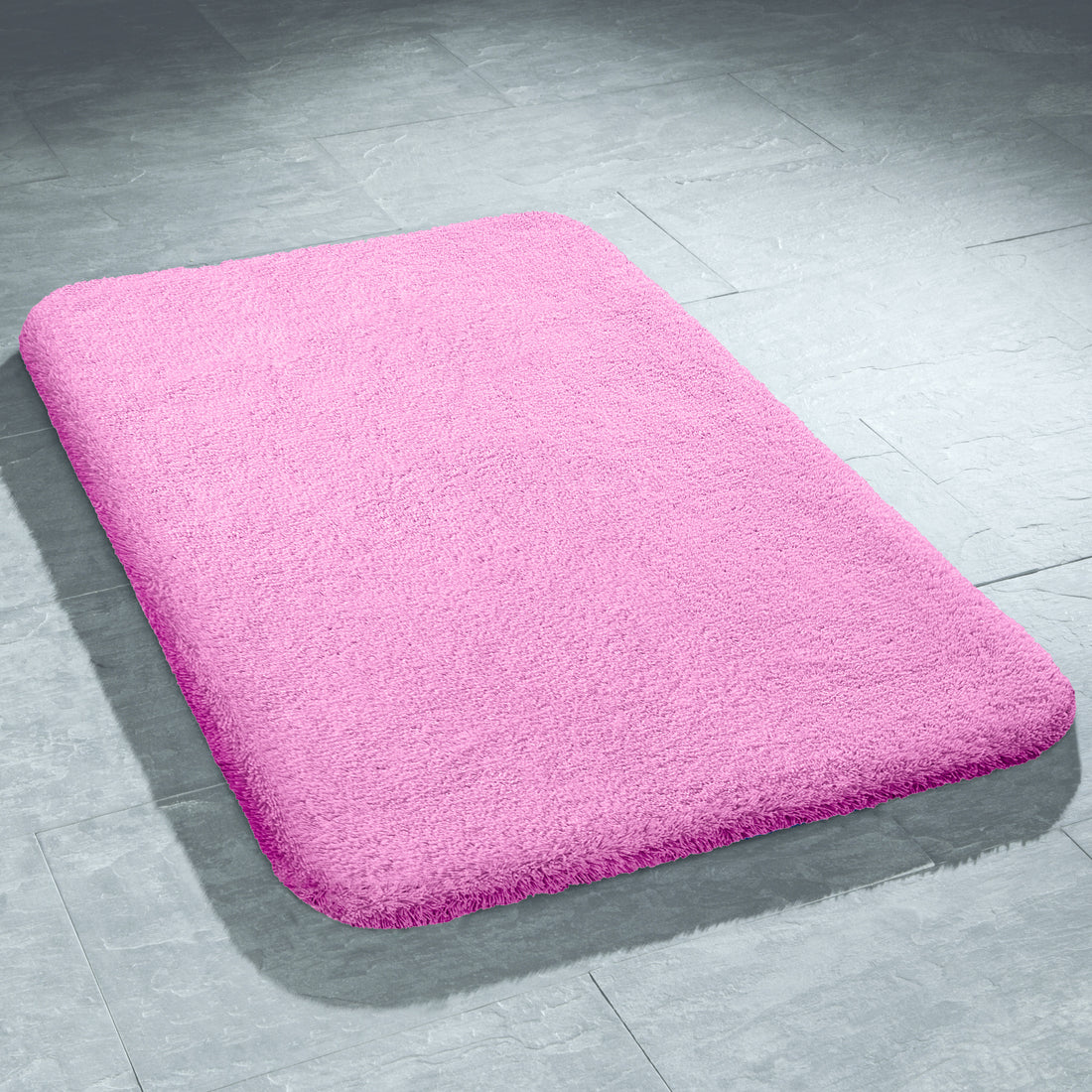 Rosa rechteckiger Badtteppich mit abgerundeten Ecken liegt auf einem hellgrauen Fliesenboden.