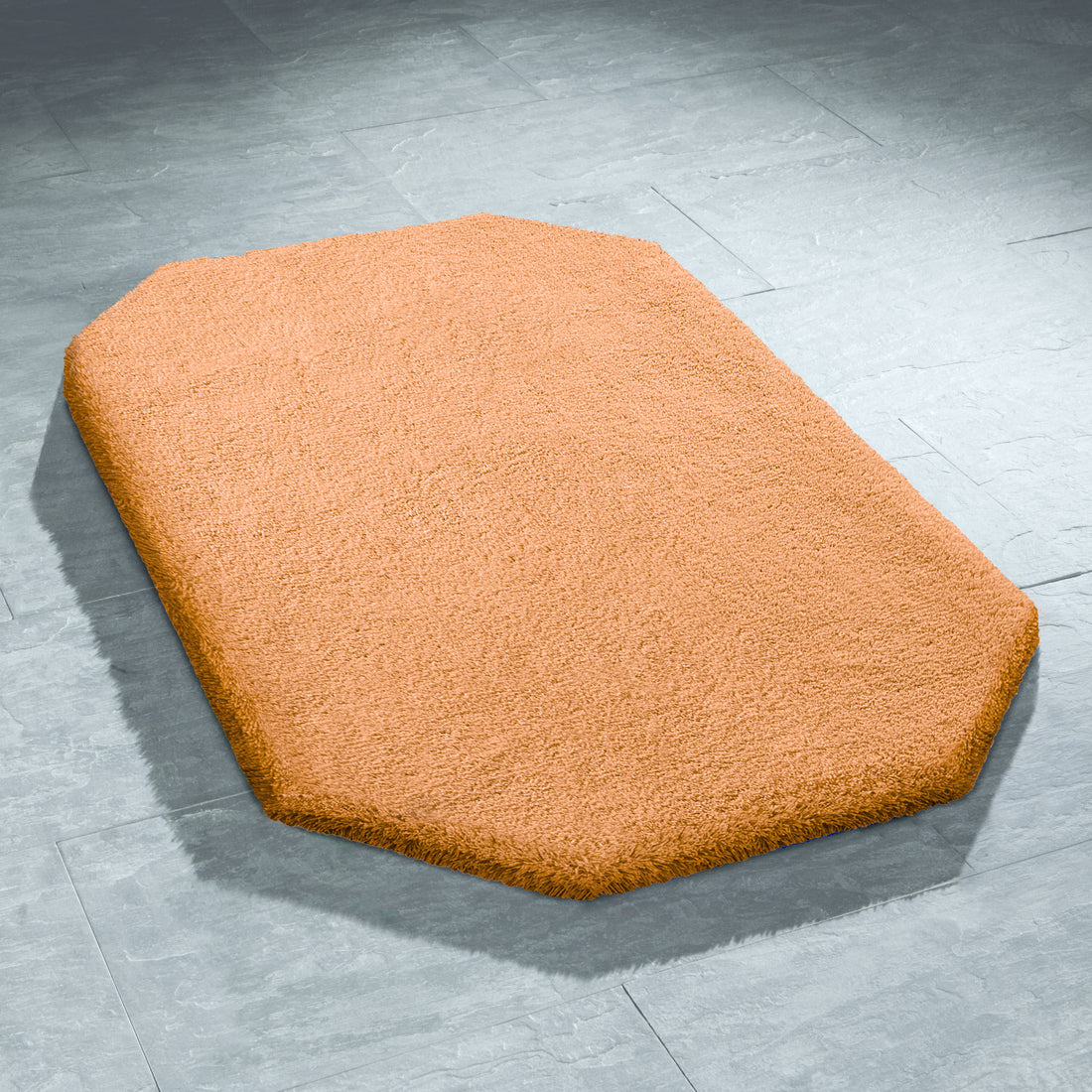 Ein achteckiger rostfarbener Badteppich Grandezza liegt auf hellgrauen Bodenfliesen.