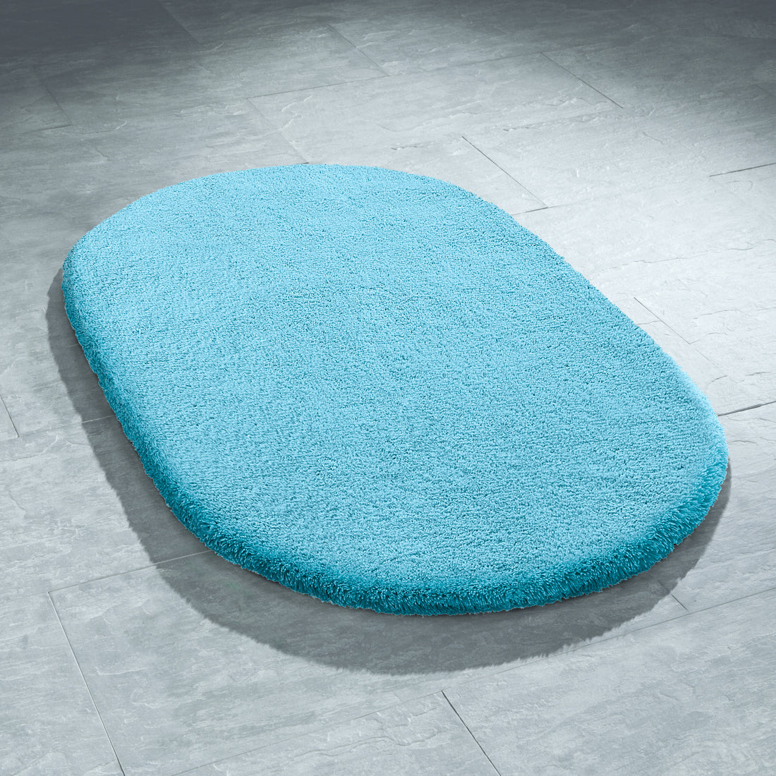 Ovaler hellblauer Kleine Wolke Badteppich auf grauem Fliesenboden im Bad.