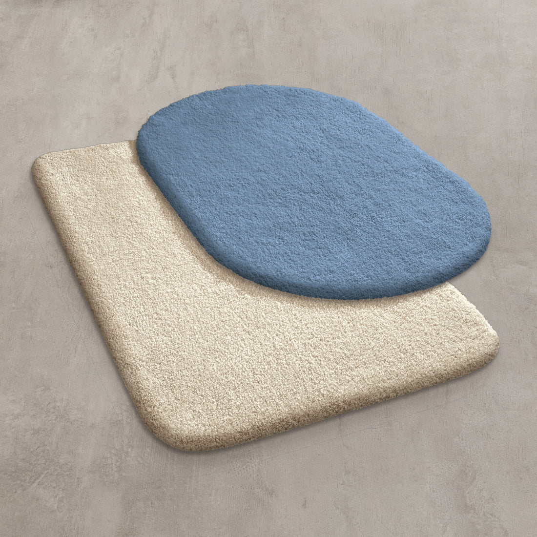 Zwei überlappende Kleine Wolke Grandezza Badematten in Beige und Blau liegen auf einem Boden.