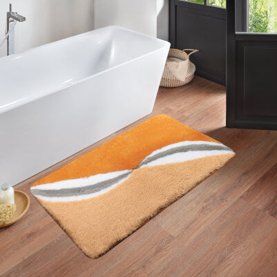 Orange-beiger Badteppich mit Wellenmuster vor freistehender Badewanne.