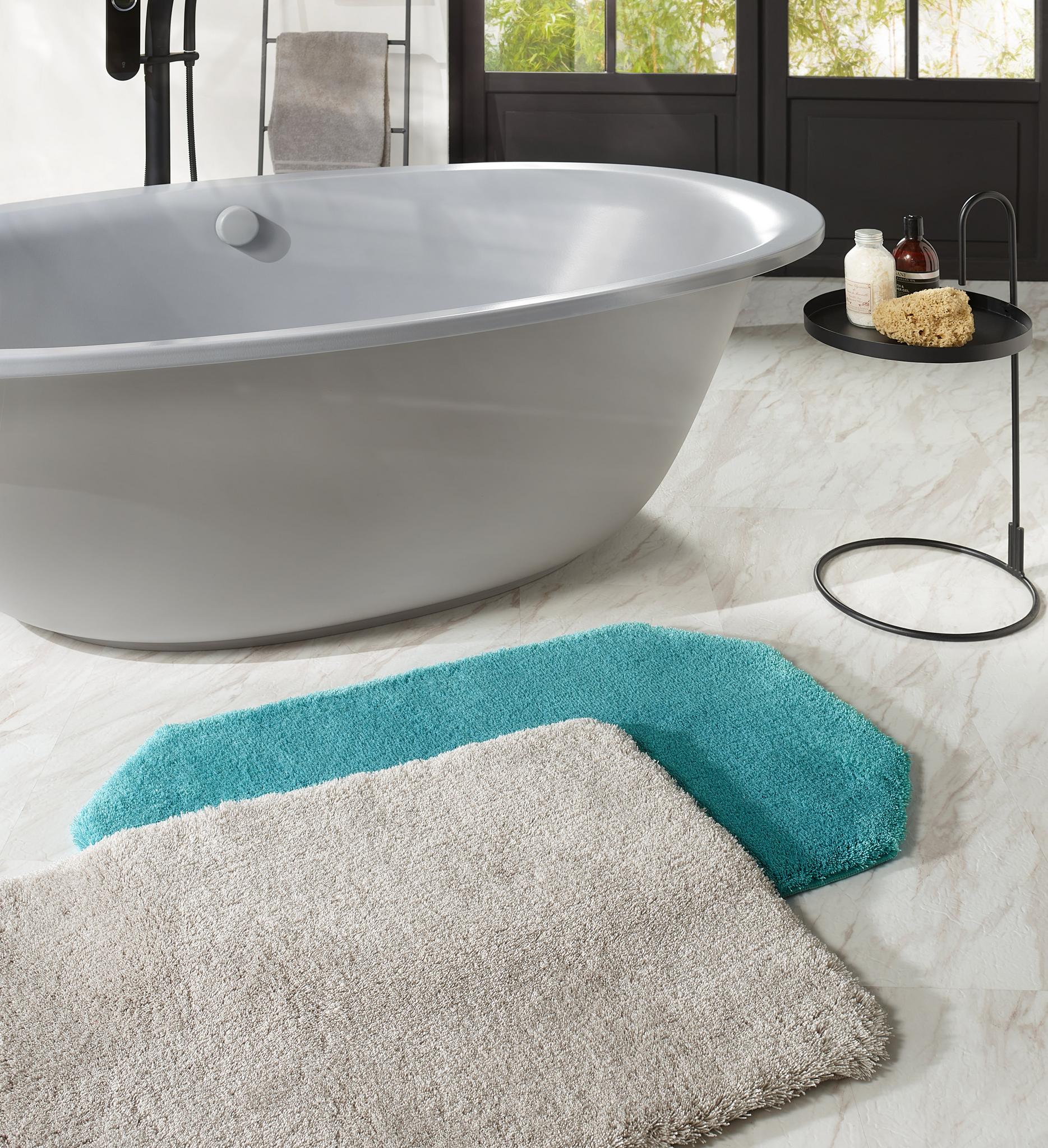 Graue Badewanne mit runden Tisch, Deko und zwei Badvorlegern auf Marmor