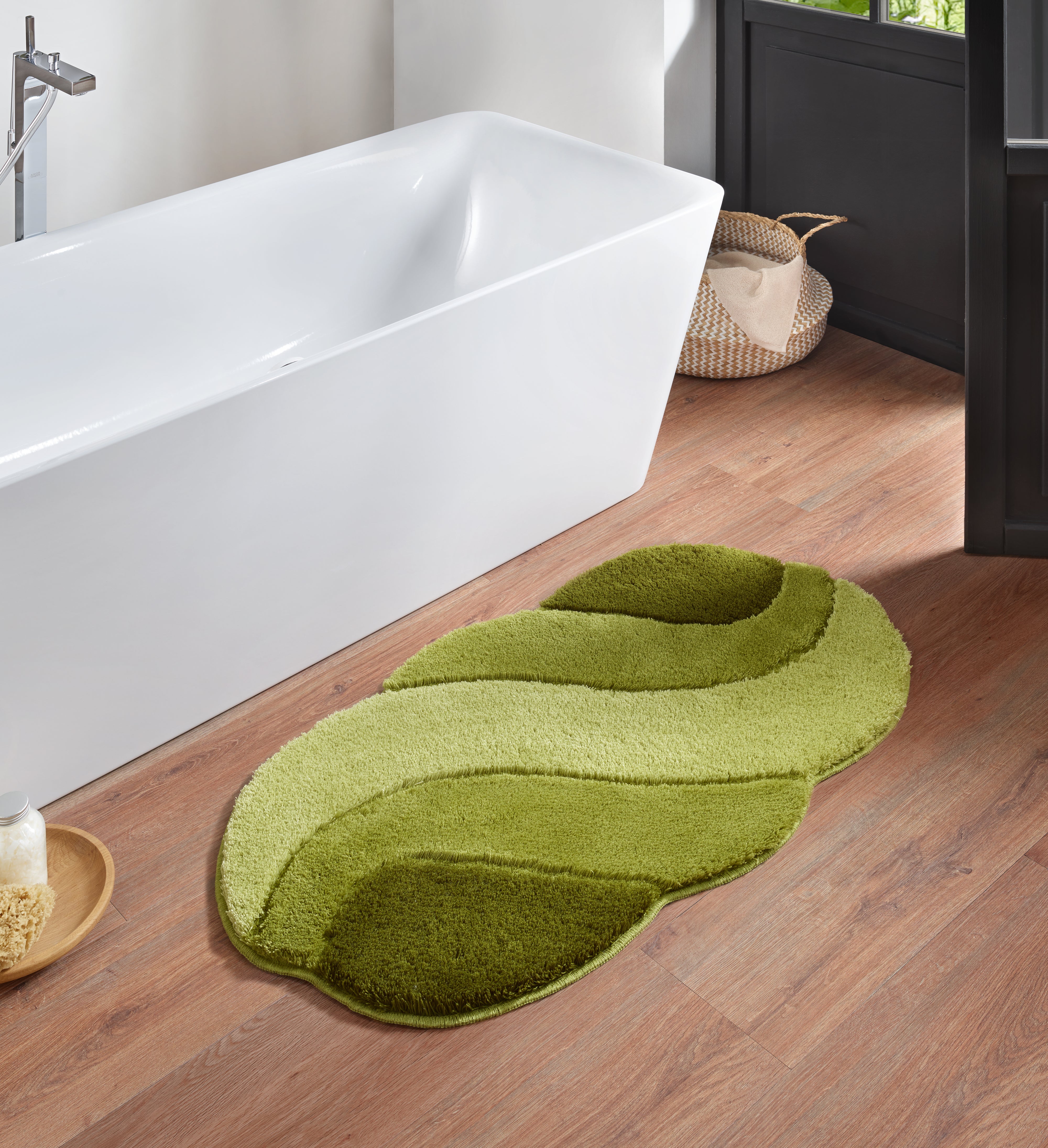 Grüner Badteppich Kleine Wolke Creativo Harmonia liegt vor einer weißen Badewanne auf Holzfußboden.