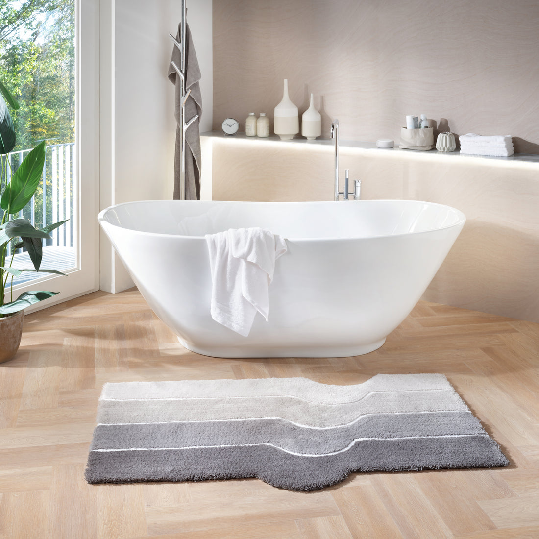 Der Kleine Wolke Creativo Badteppich liegt vor einer freistehenden Badewanne im hellen Bad.