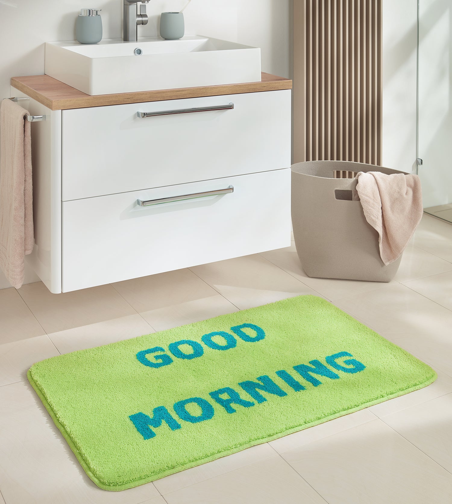 Grüne Kleine Wolke Badematte mit blauem GOOD MORNING Schriftzug in modernem Badezimmer vor Waschbecken.