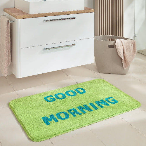Grüne Badematte mit blauem Schriftzug GOOD MORNING vor Waschbecken