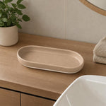 Eine beige, ovale Ablageschale steht auf einem Holzwaschtisch.