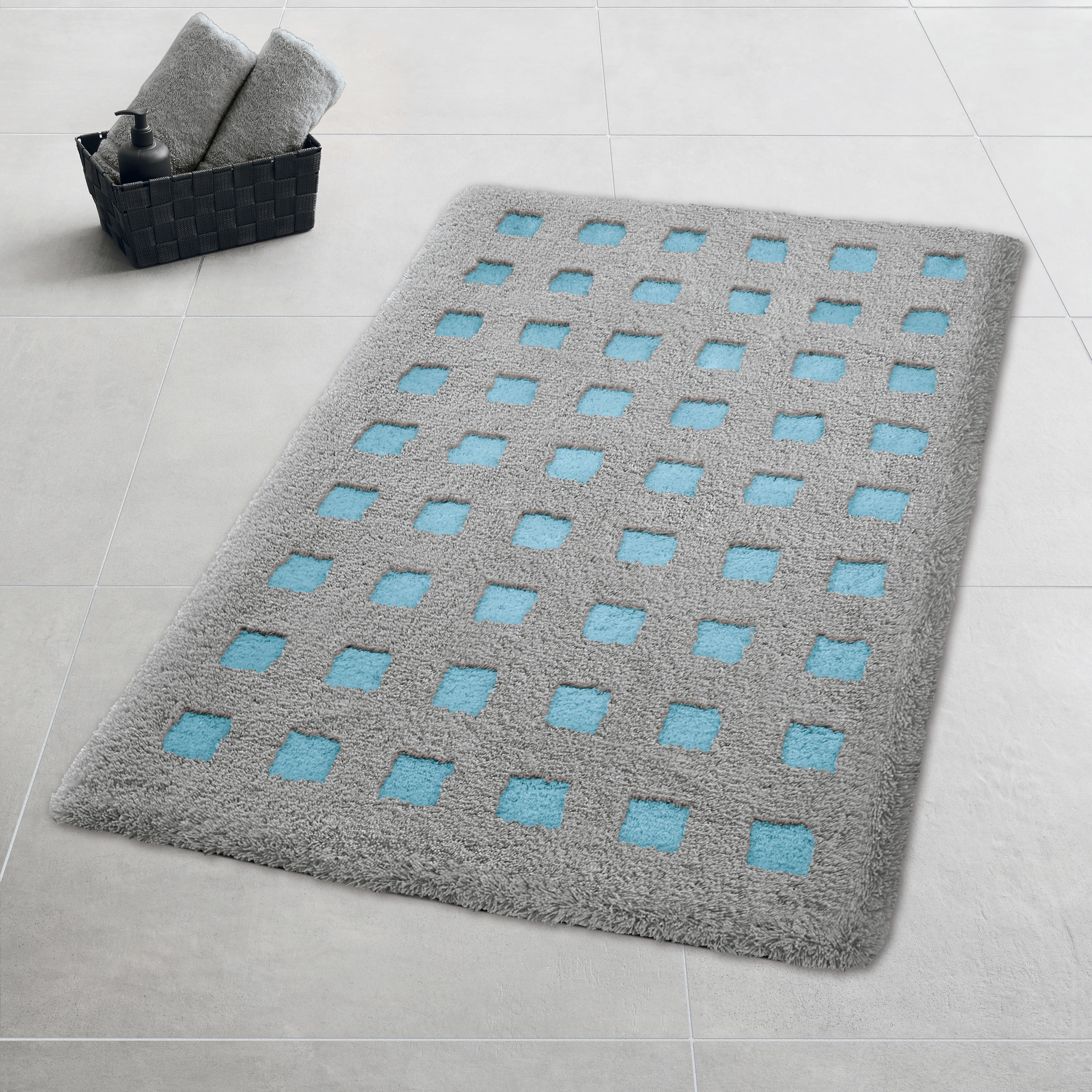 Graue Kleine Wolke Badematte Aqua et Noir mit blauen Quadraten auf Fliesenboden neben Handtuchkorb.
