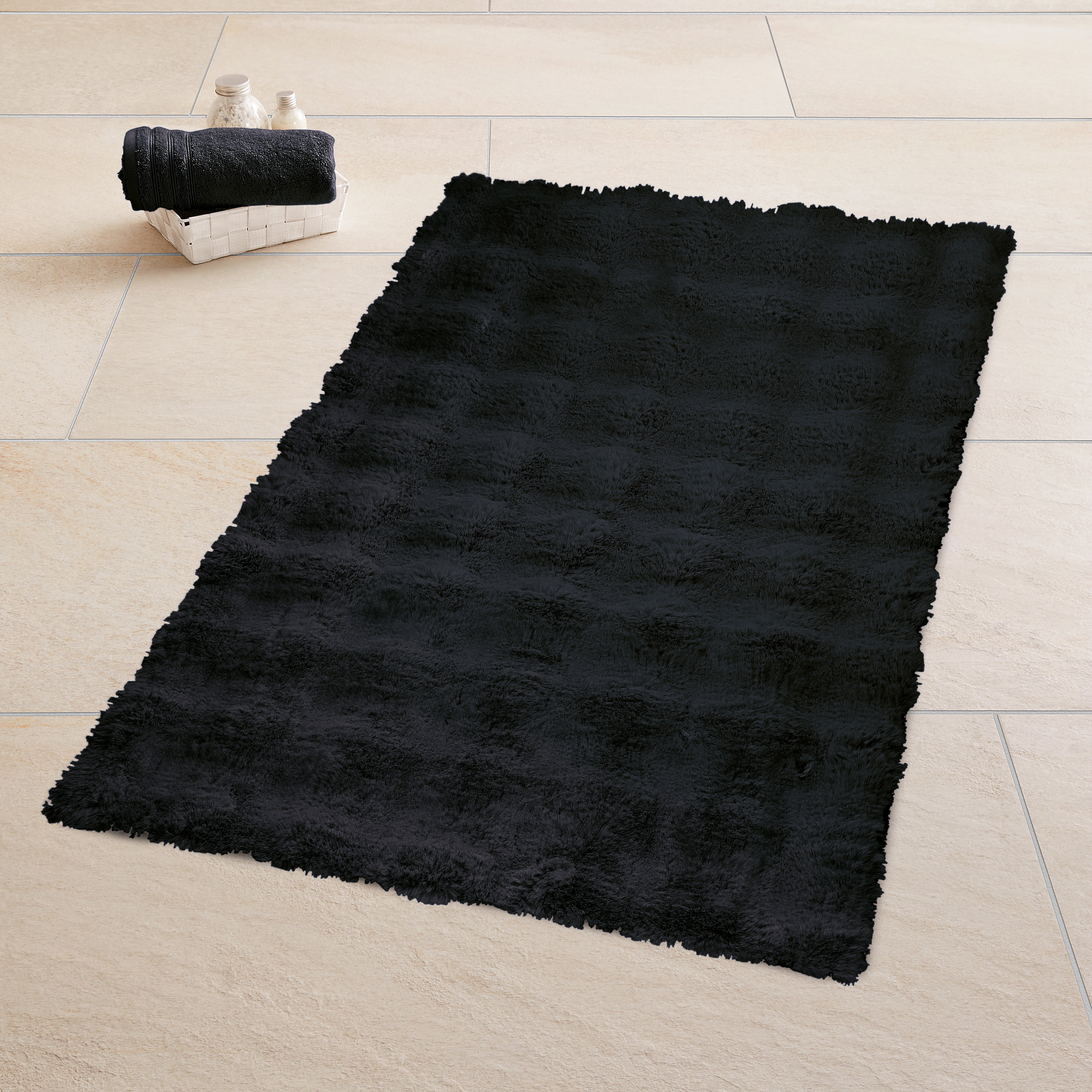 Schwarzer Badteppich liegt auf hellem Fliesenboden neben Korb mit Handtuch und Badaccessoires.