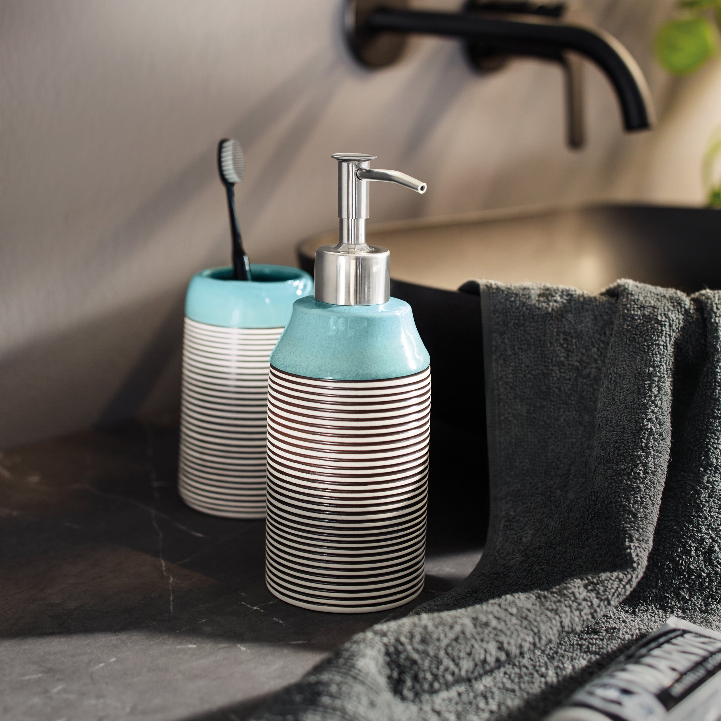 Kleine Wolke Seifenspender und Zahnputzbecher Aqua et Noir Okapi stehen auf einem Waschtisch im Bad.