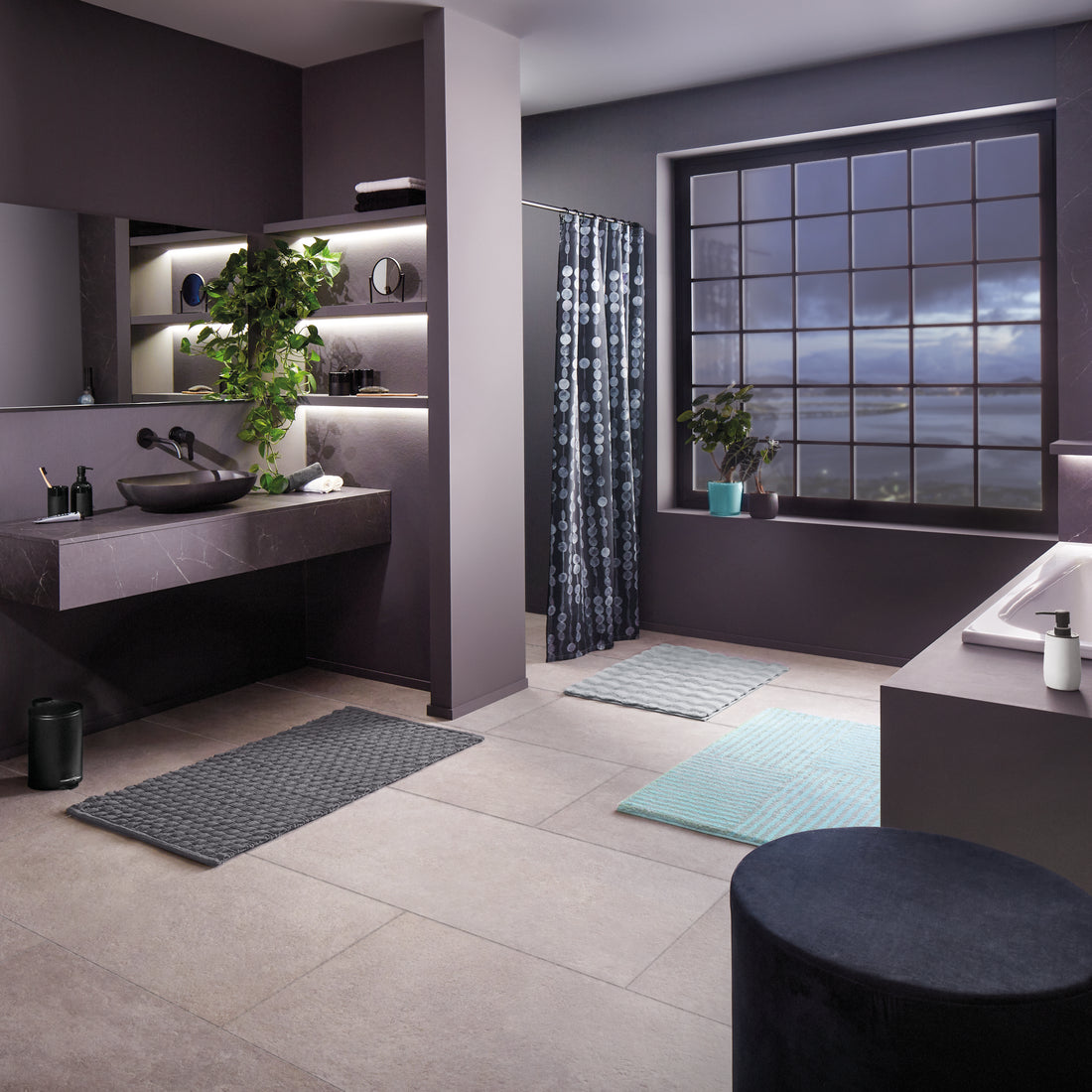 In einem modernen Bad liegen mehrere Badteppiche in Grau und Aqua vor Dusche und Wanne.