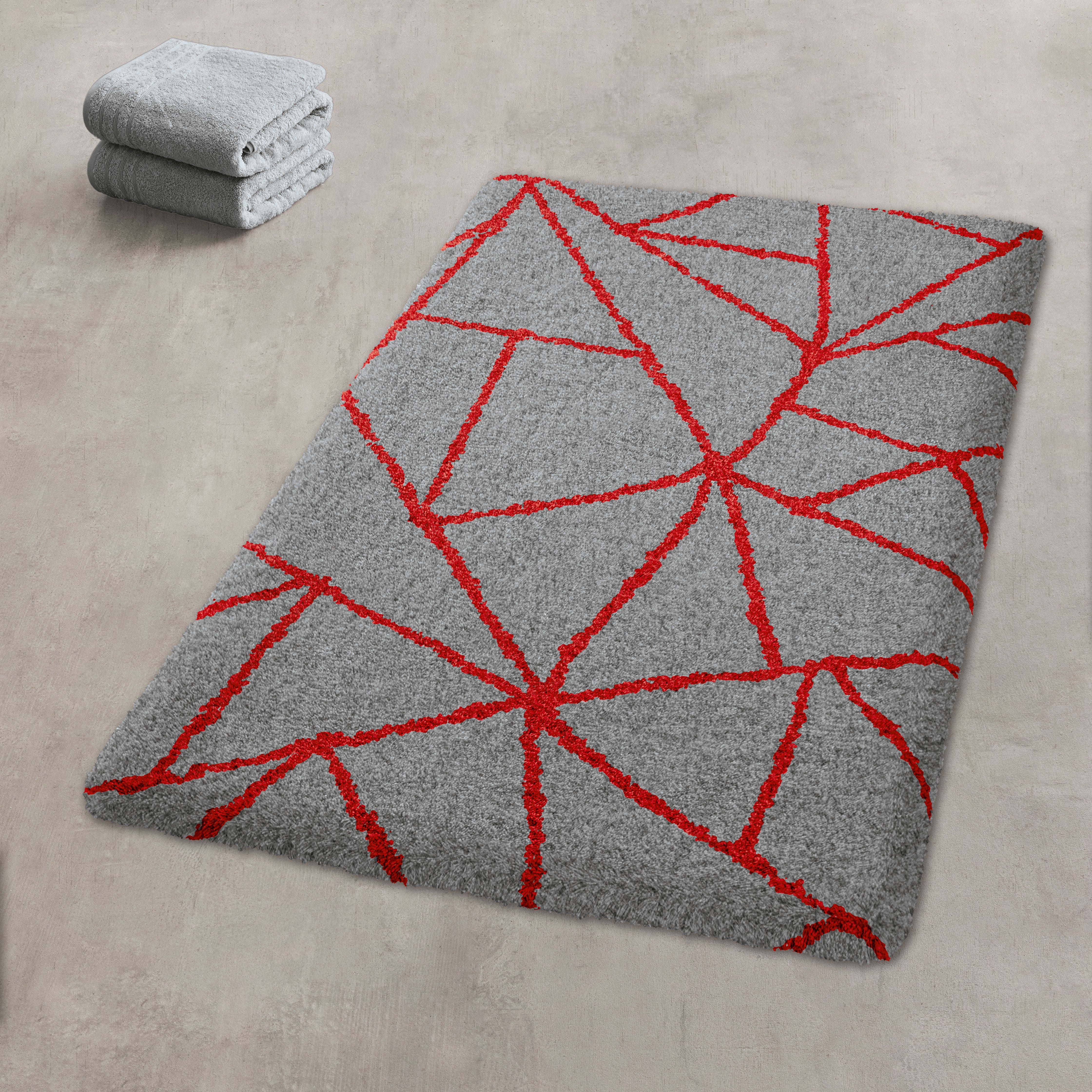 Graue Badematte Dynamic Red von Kleine Wolke mit roten Linien und grauen Handtüchern auf Betonboden.