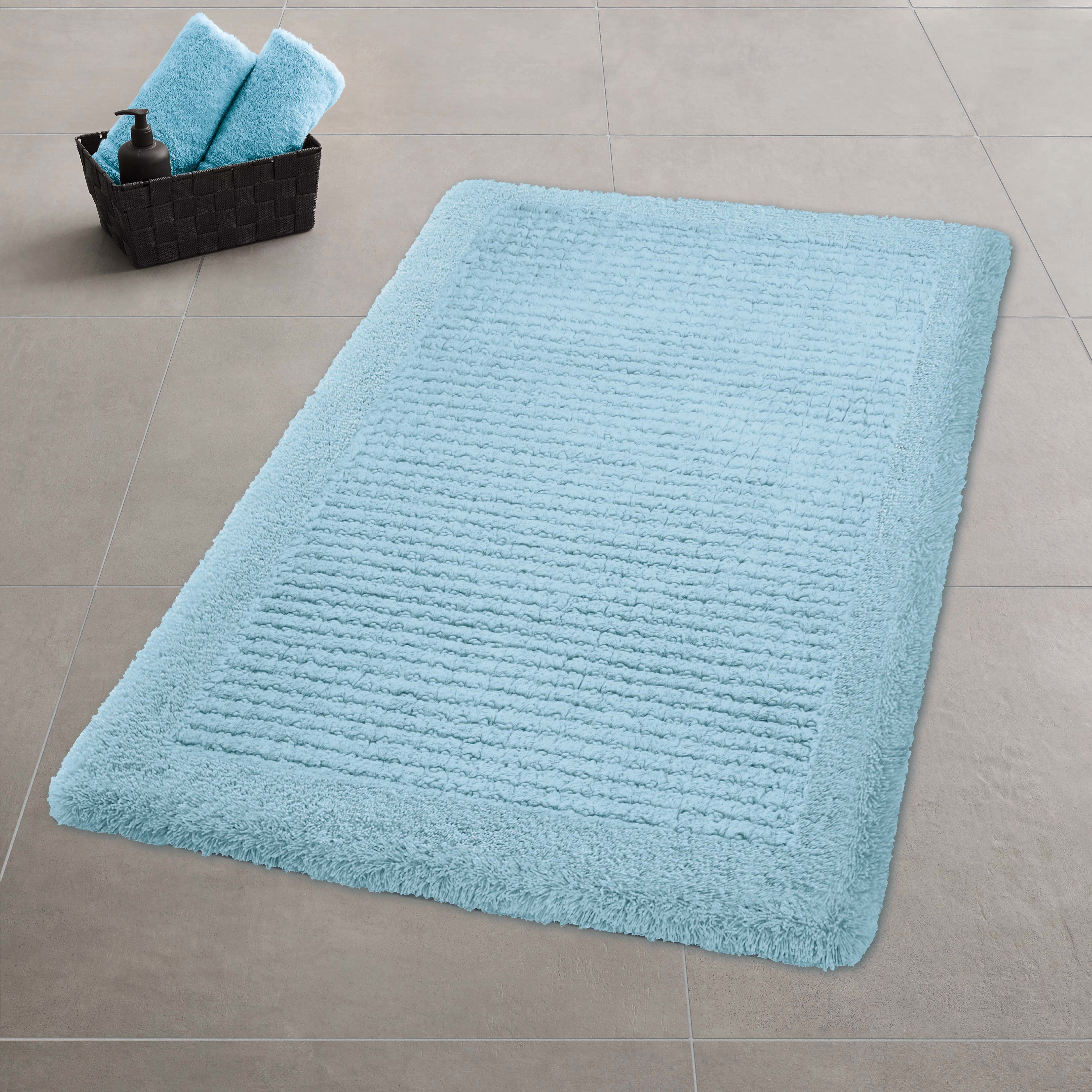 Hellblauer Kleine Wolke Badteppich liegt auf grauen Fliesen neben Korb mit Handtüchern und Spender.