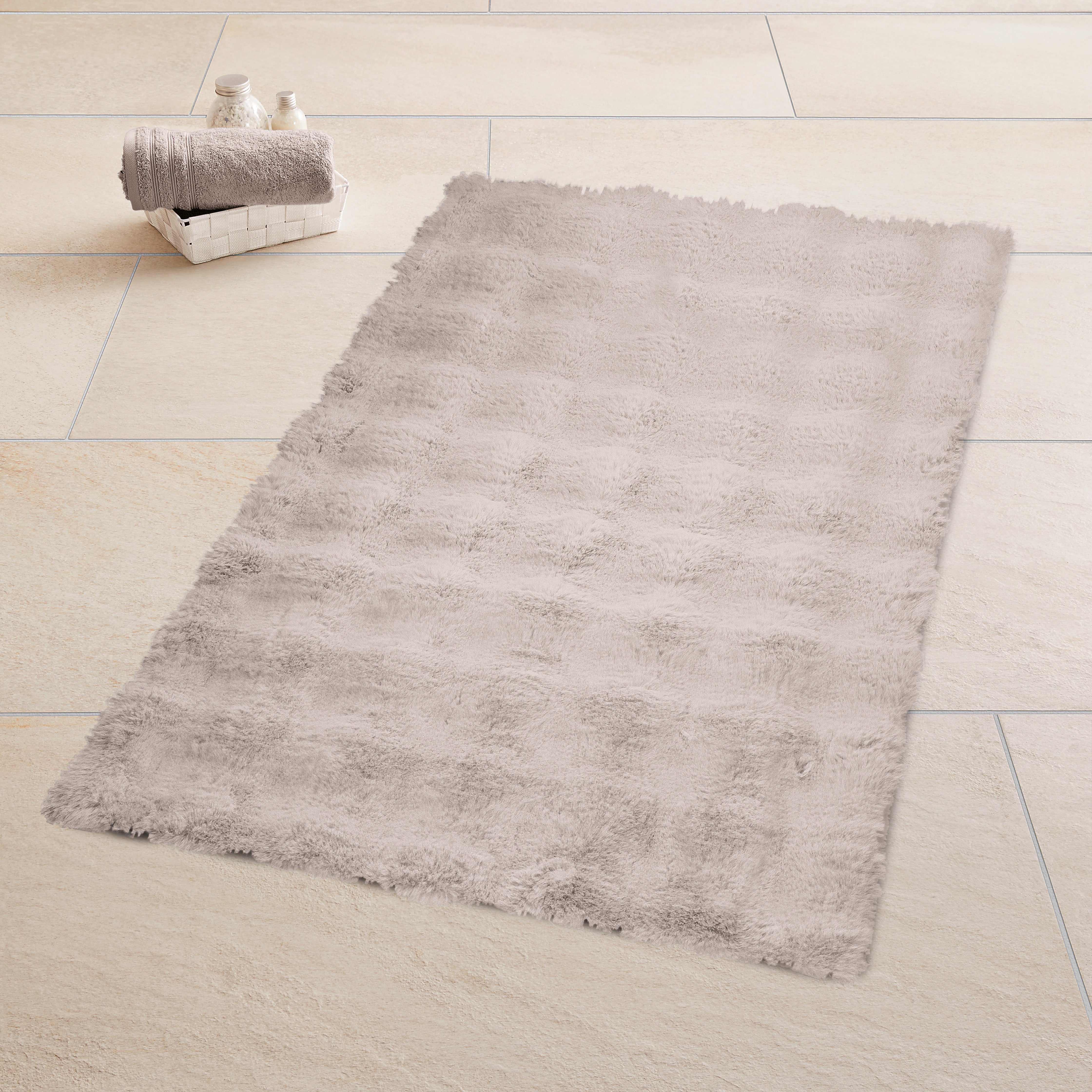 Weicher Kleine Wolke Badteppich in hellem Beige liegt auf großen Fliesen neben Korb mit Handtüchern.