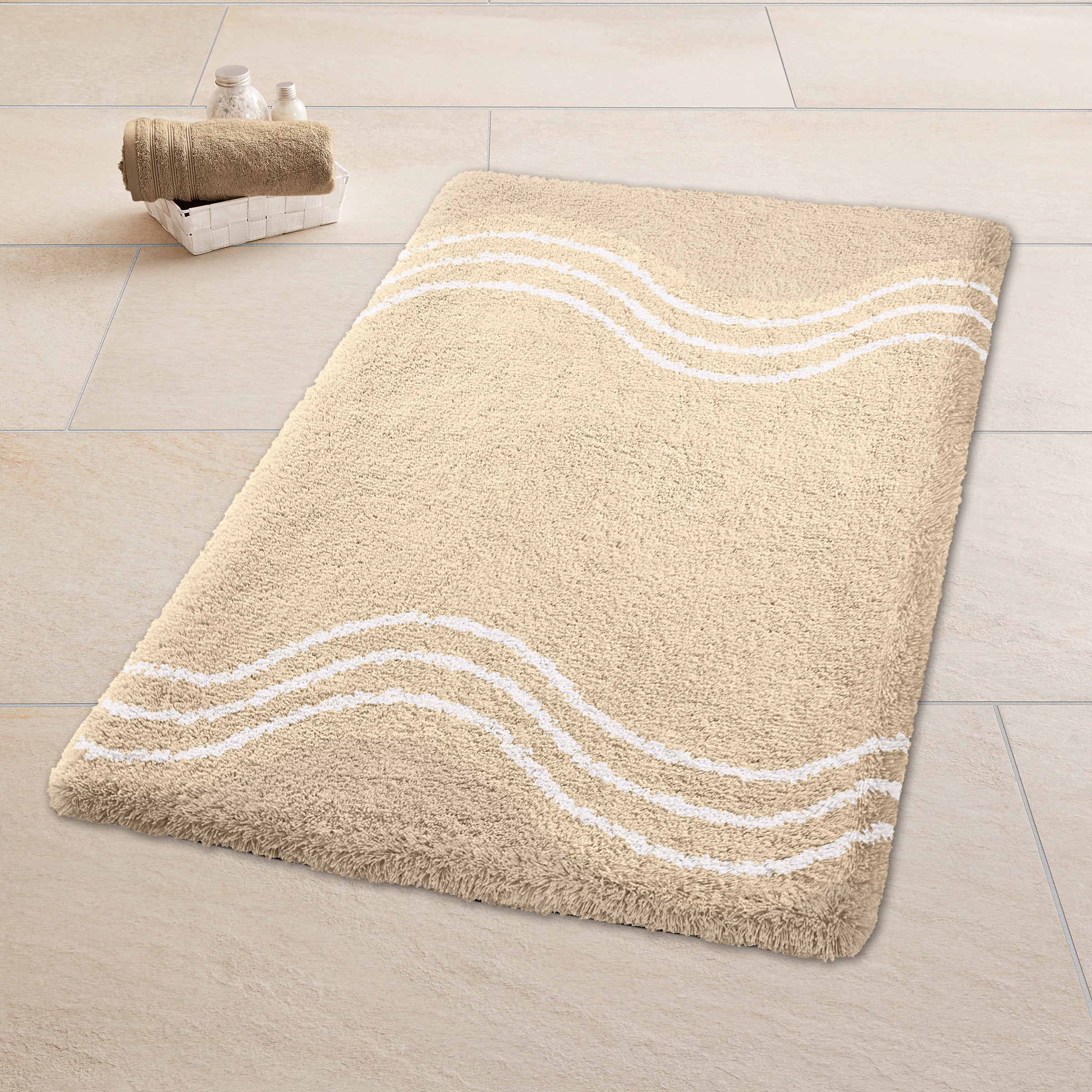Beige Badematte mit weißen Wellenlinien liegt auf hellen Fliesen neben Korb mit Handtuch.