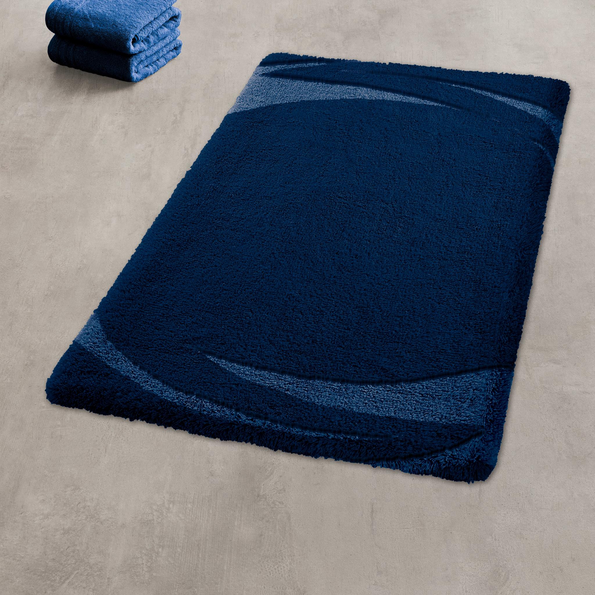 Blauer Badteppich mit geschwungenem Muster neben gefalteten Handtüchern