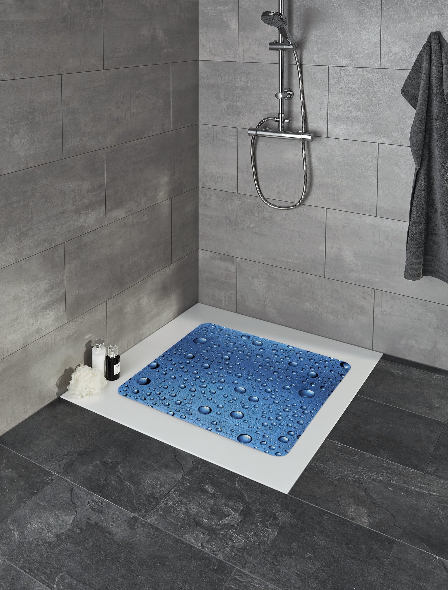 Marineblaue Duscheinlage BUBBLE 55 x 55 cm liegt in einer grau gefliesten Dusche mit Dekoartikeln.